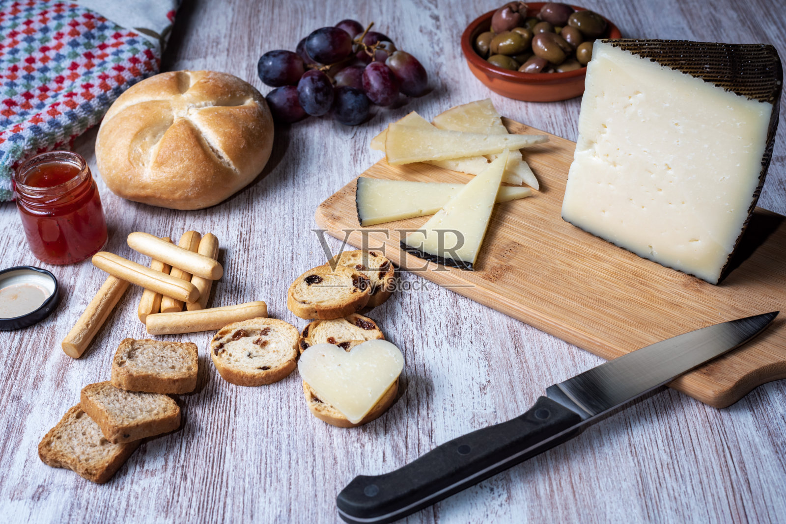 切菜板上有一块奶酪，配上葡萄、果酱、橄榄和什锦面包。照片摄影图片