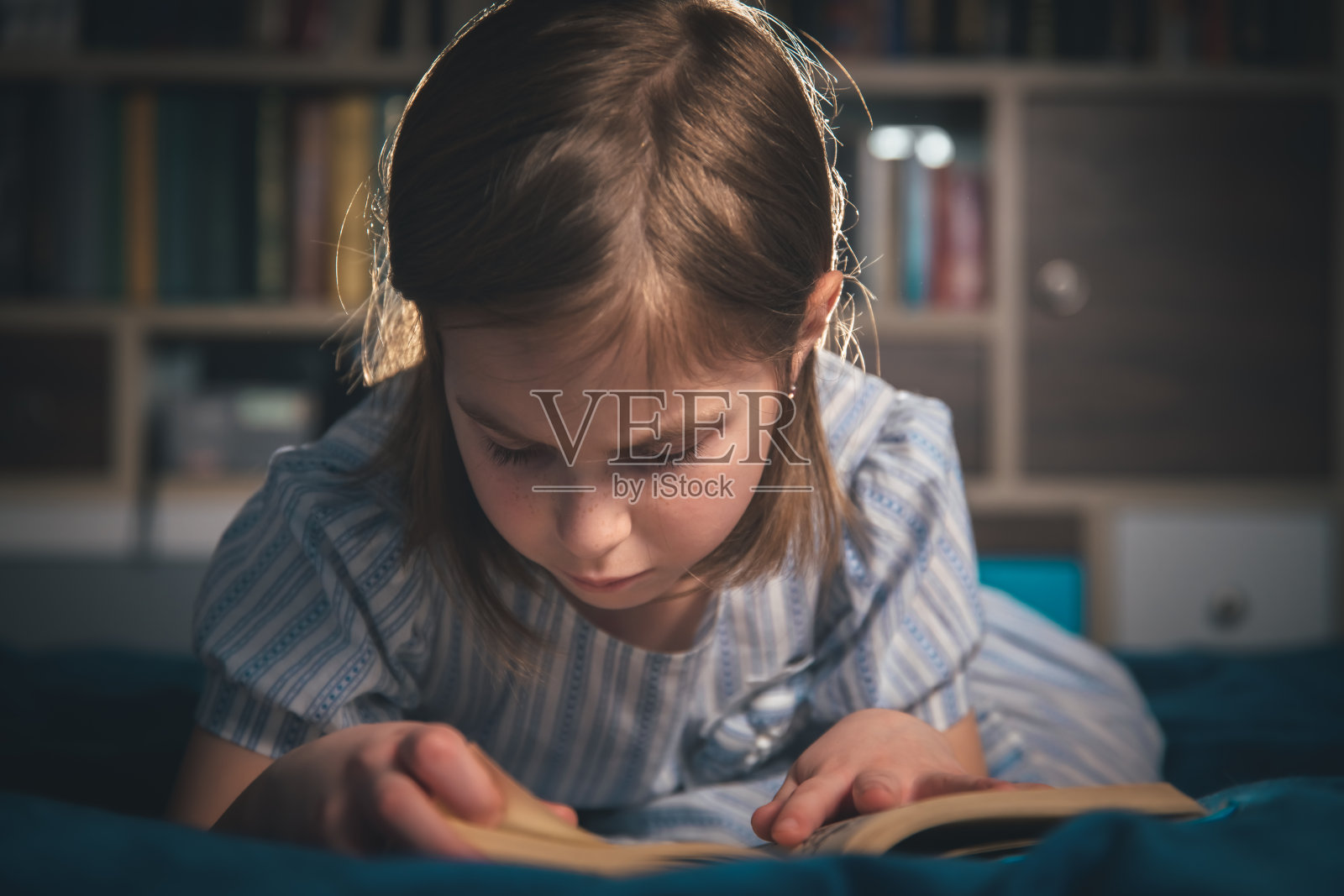 可爱的女孩在家里看书，躺在床上照片摄影图片