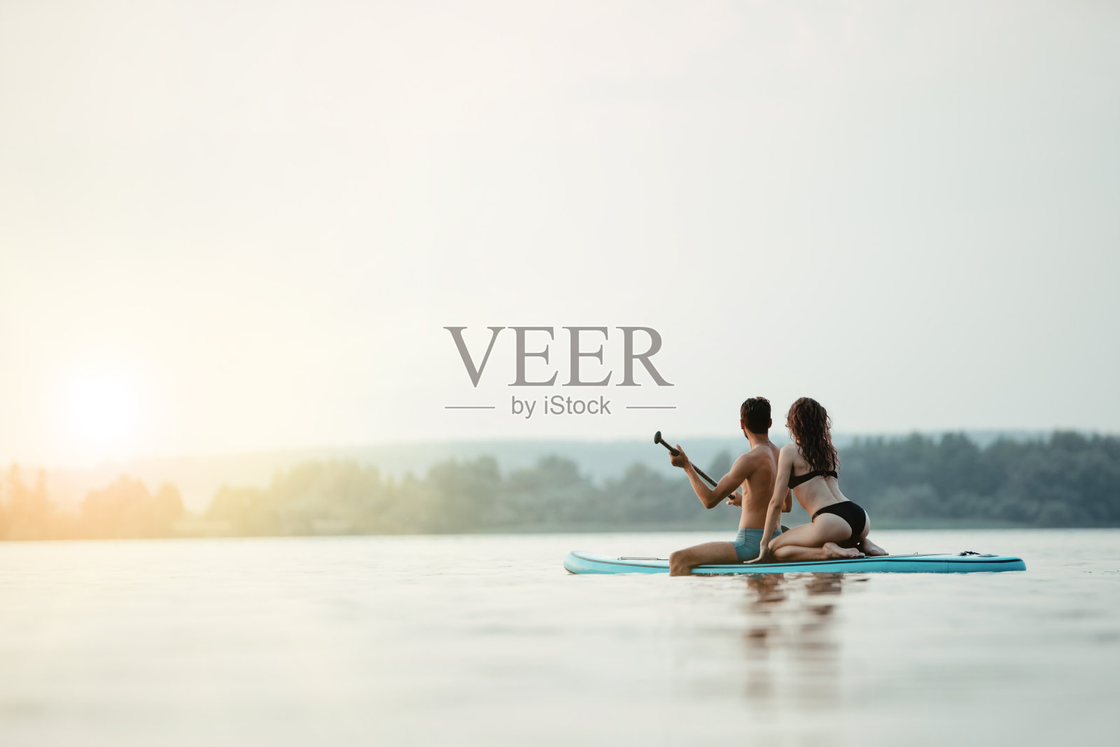 一对年轻的夫妇沿着河散步，坐在SAP板上照片摄影图片