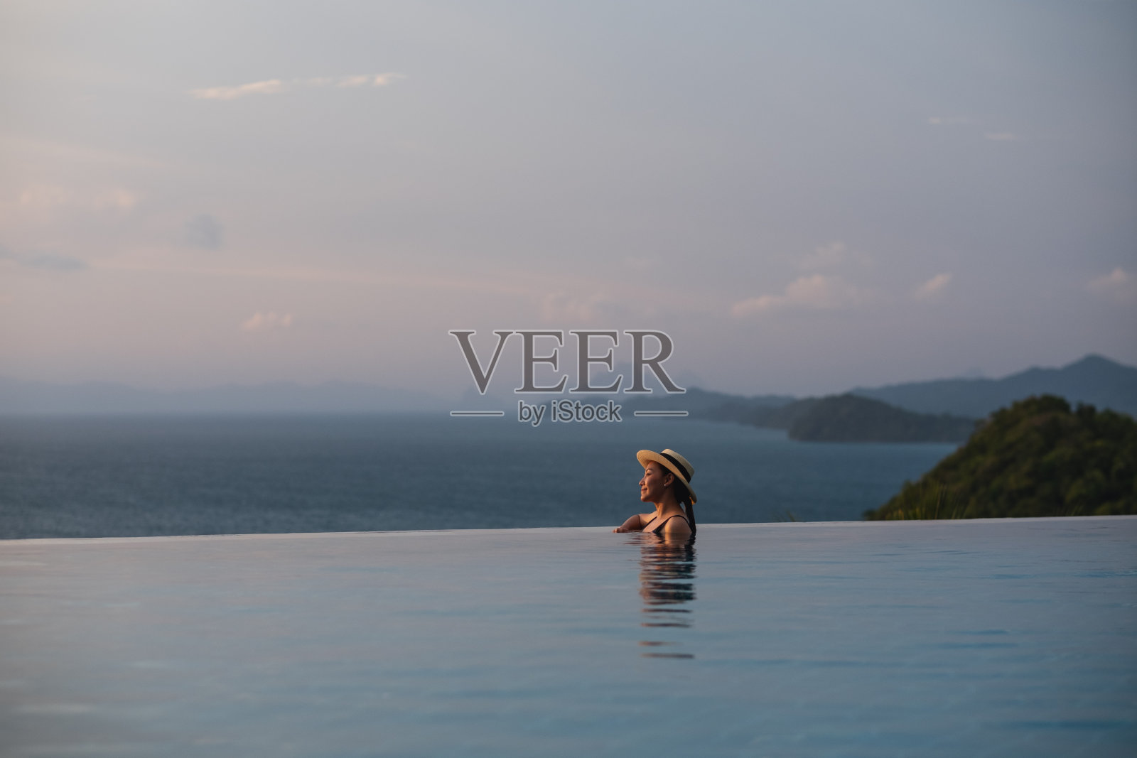 一个年轻的女人放松在无限游泳池与美丽的岛屿和海景照片摄影图片