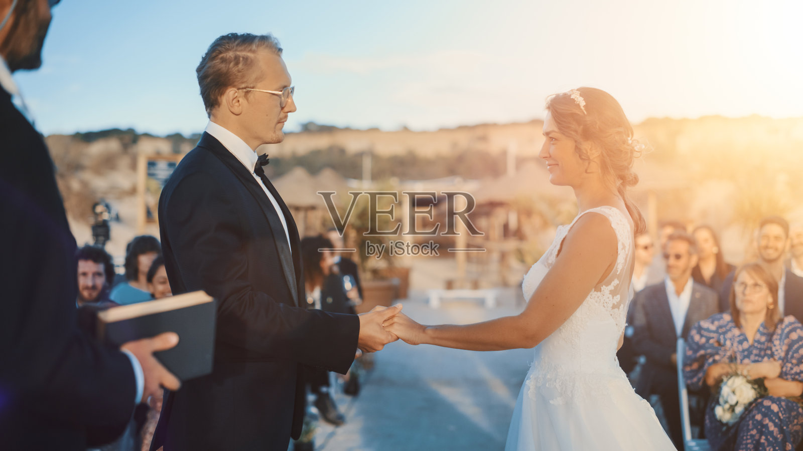 美丽的新娘和新郎在户外婚礼上在海洋海滩日落。完美的地方，一对夫妇结婚，交换戒指，亲吻和分享庆祝活动与多民族的朋友。照片摄影图片