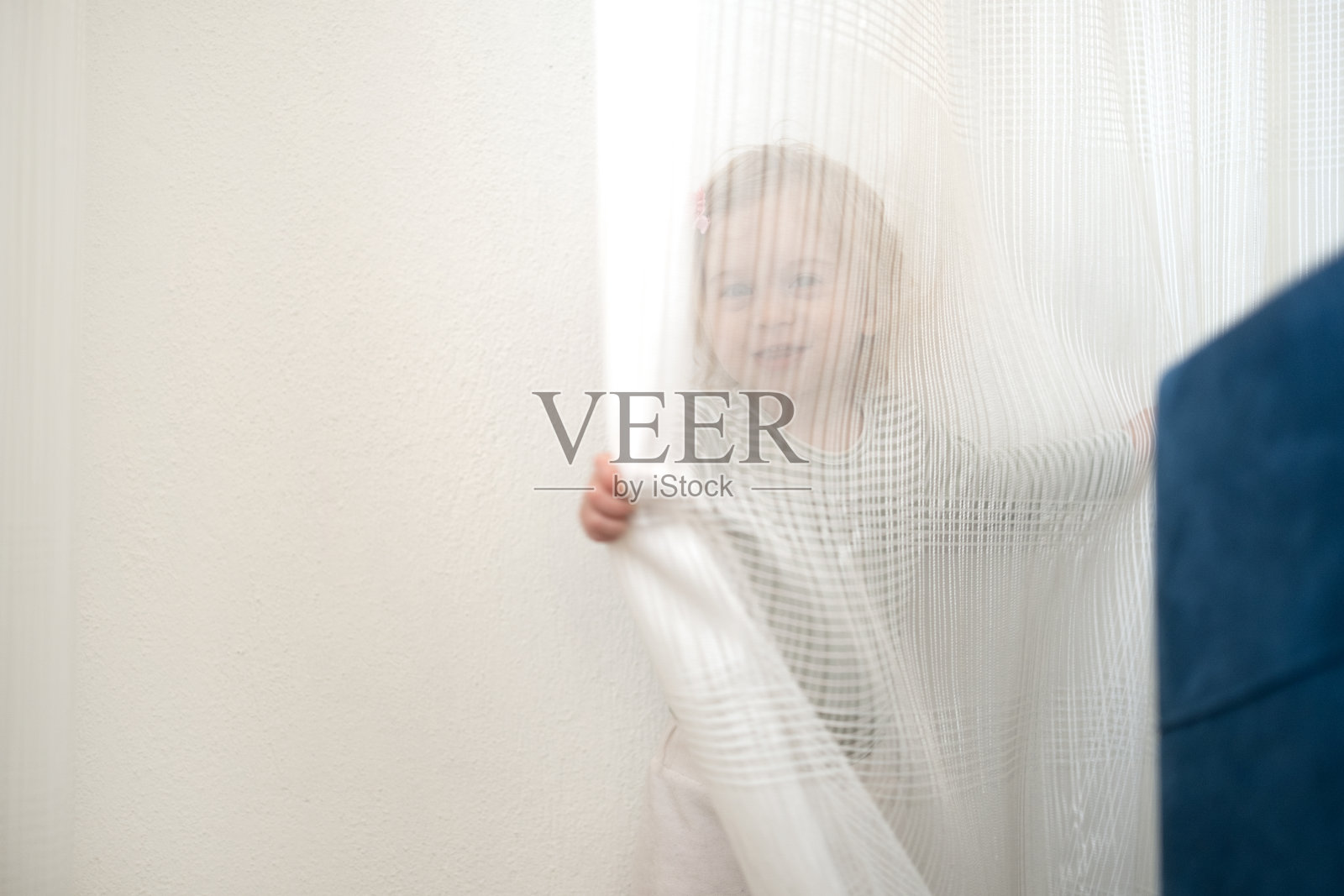 可爱的1、2岁的白种人金发女孩玩，躲在窗帘后面，在家里的灯光室内看着相机玩得很开心。孩子，孩子，幼儿室内游戏，大笑，微笑的婴儿。本空间照片摄影图片