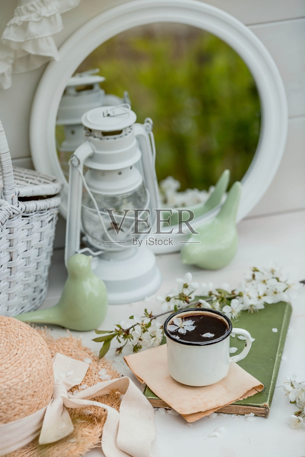 视觉内容。复古风格的静物。一杯咖啡，一本旧书，一顶草帽和花园里木桌上的一朵樱花。照片摄影图片