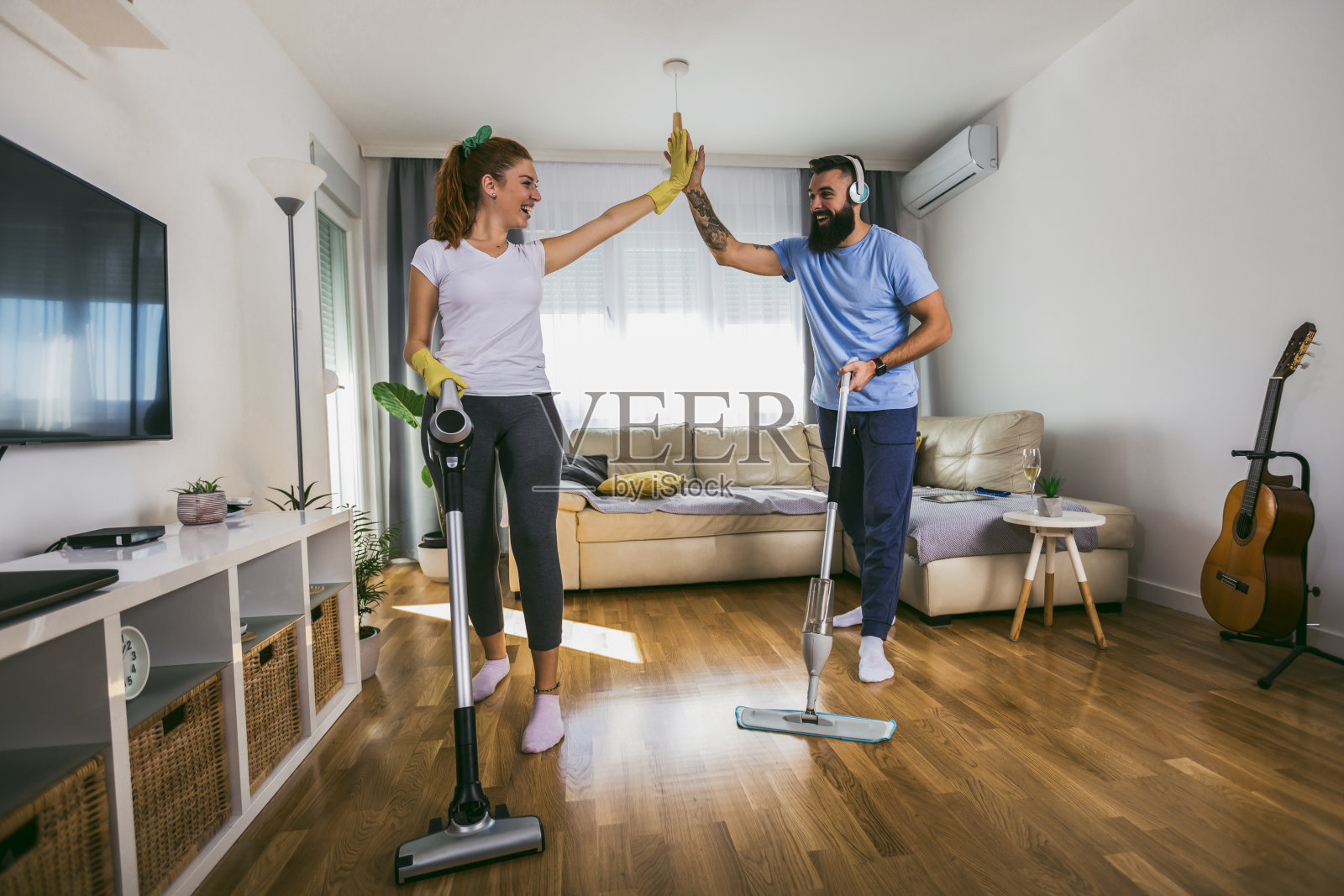 微笑着兴奋的年轻家庭主妇和她的丈夫玩吸尘器照片摄影图片