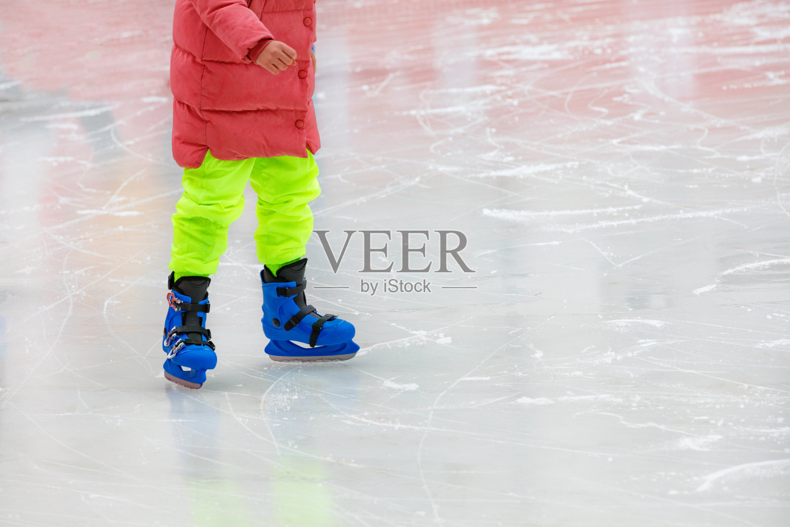 一个穿着鲜艳衣服的少年正在冰场溜冰。照片摄影图片