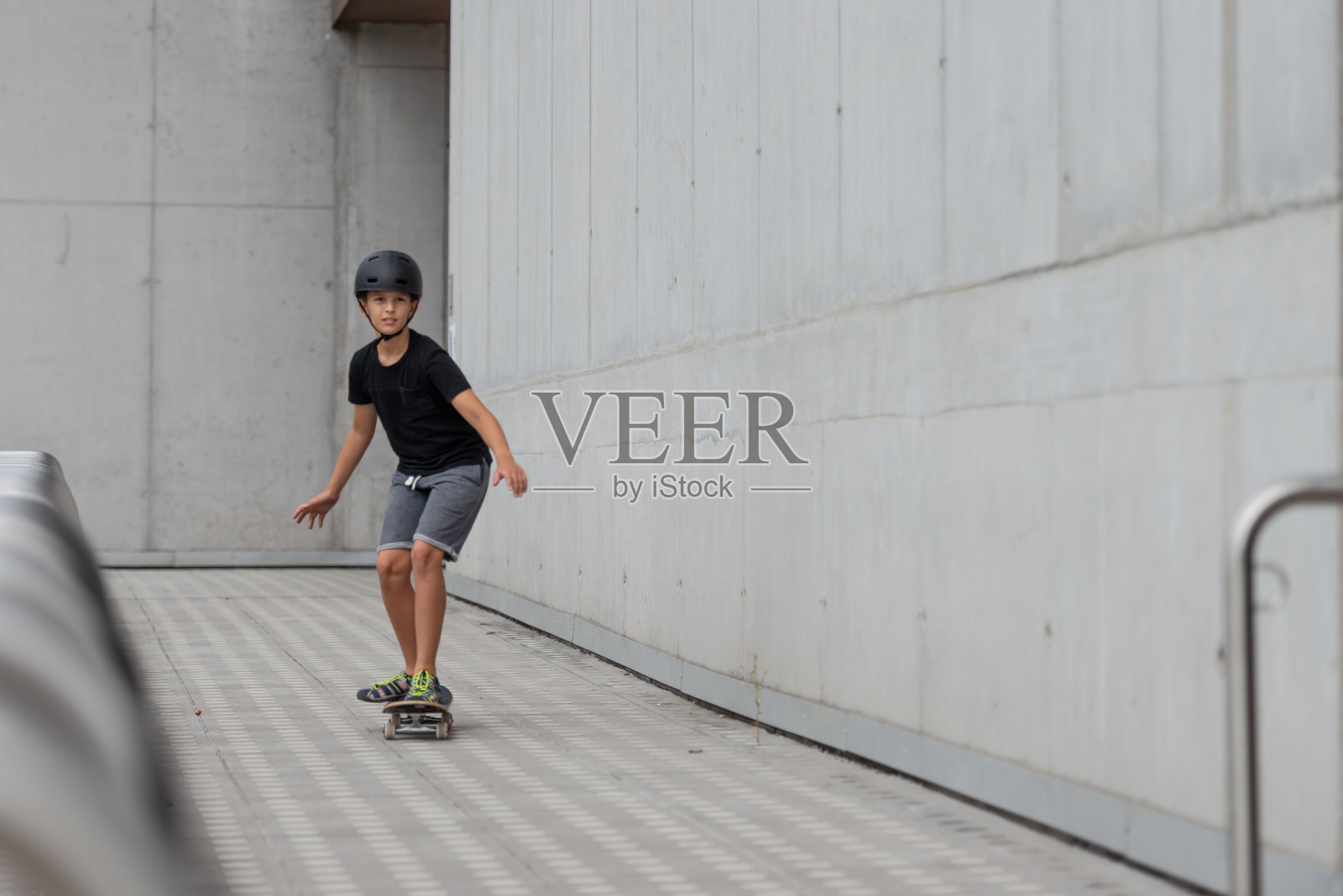 戴着头盔的黑发少女在混凝土建筑前的站台上玩滑板照片摄影图片