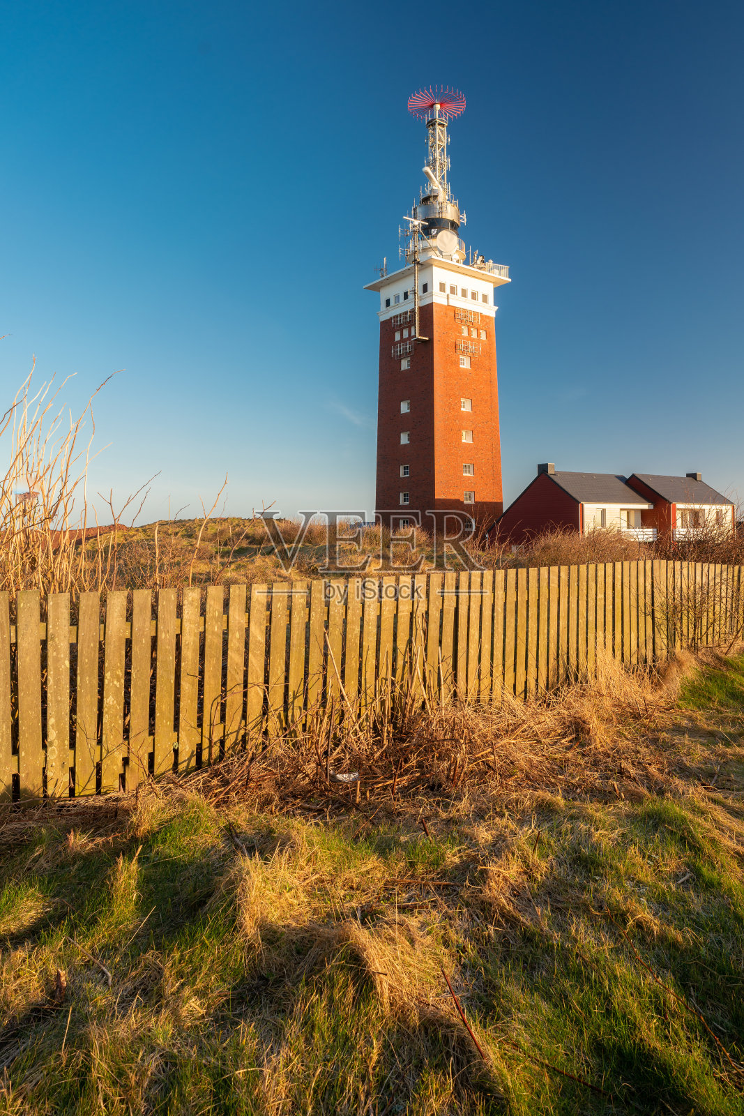 德国黑尔戈兰岛灯塔旁的黄金时间。前面是清澈的蓝天和古老的木栅栏。探索德国群岛。照片摄影图片