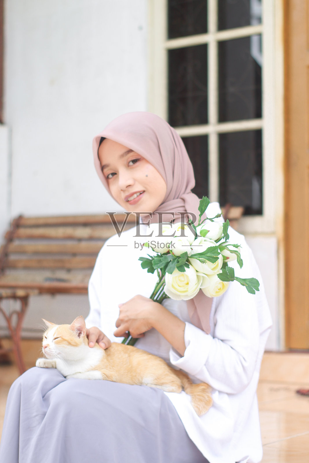 年轻的女人在房子前面和一只宠物猫玩耍照片摄影图片