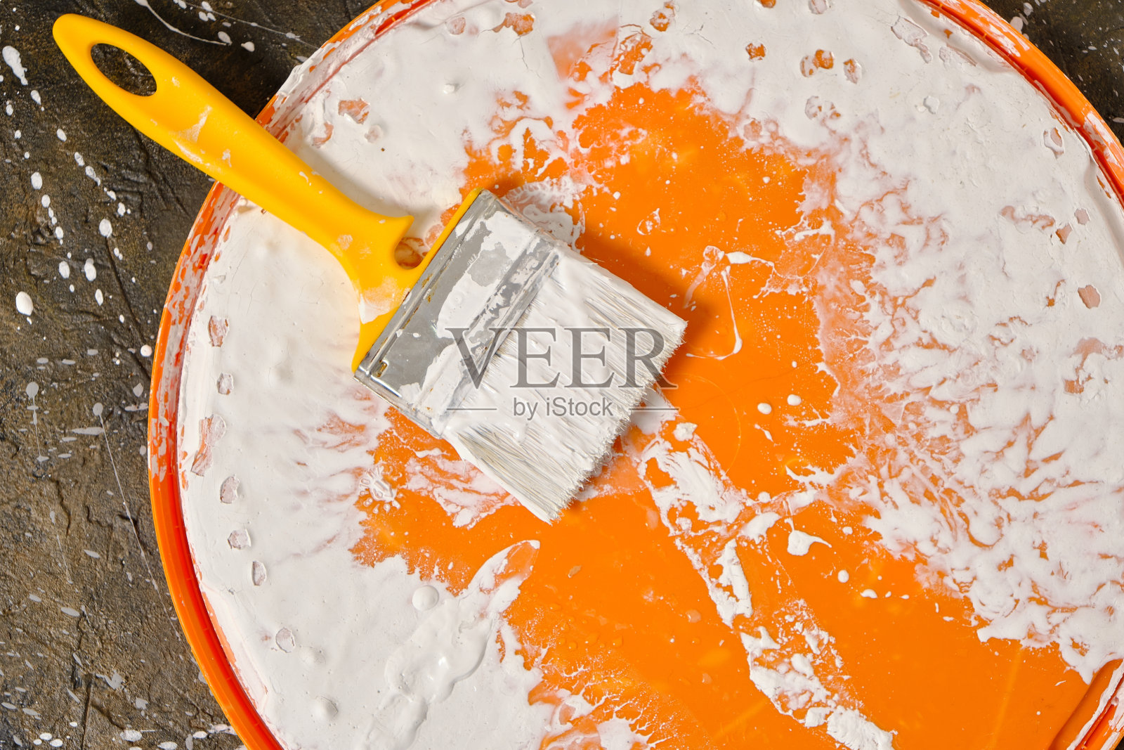 沾上油漆的脏画笔躺在地板上的橙色盖子上。照片摄影图片