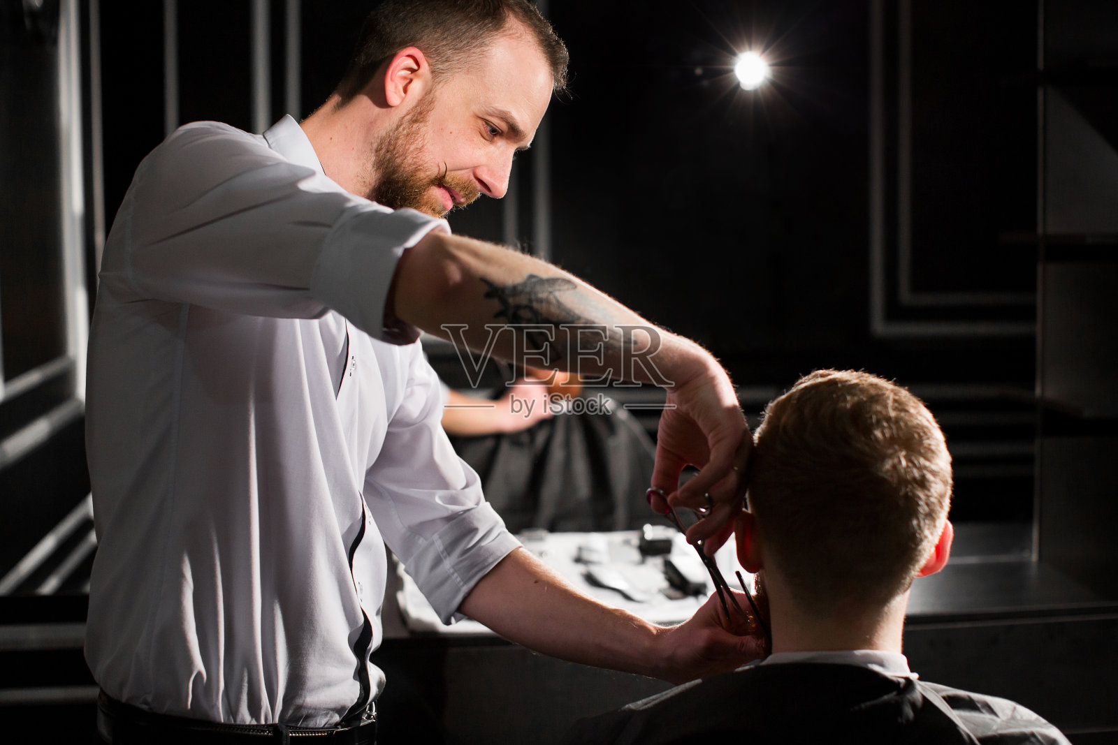 主人在理发店理发和刮胡子。理发师用剪刀和金属梳子做发型照片摄影图片