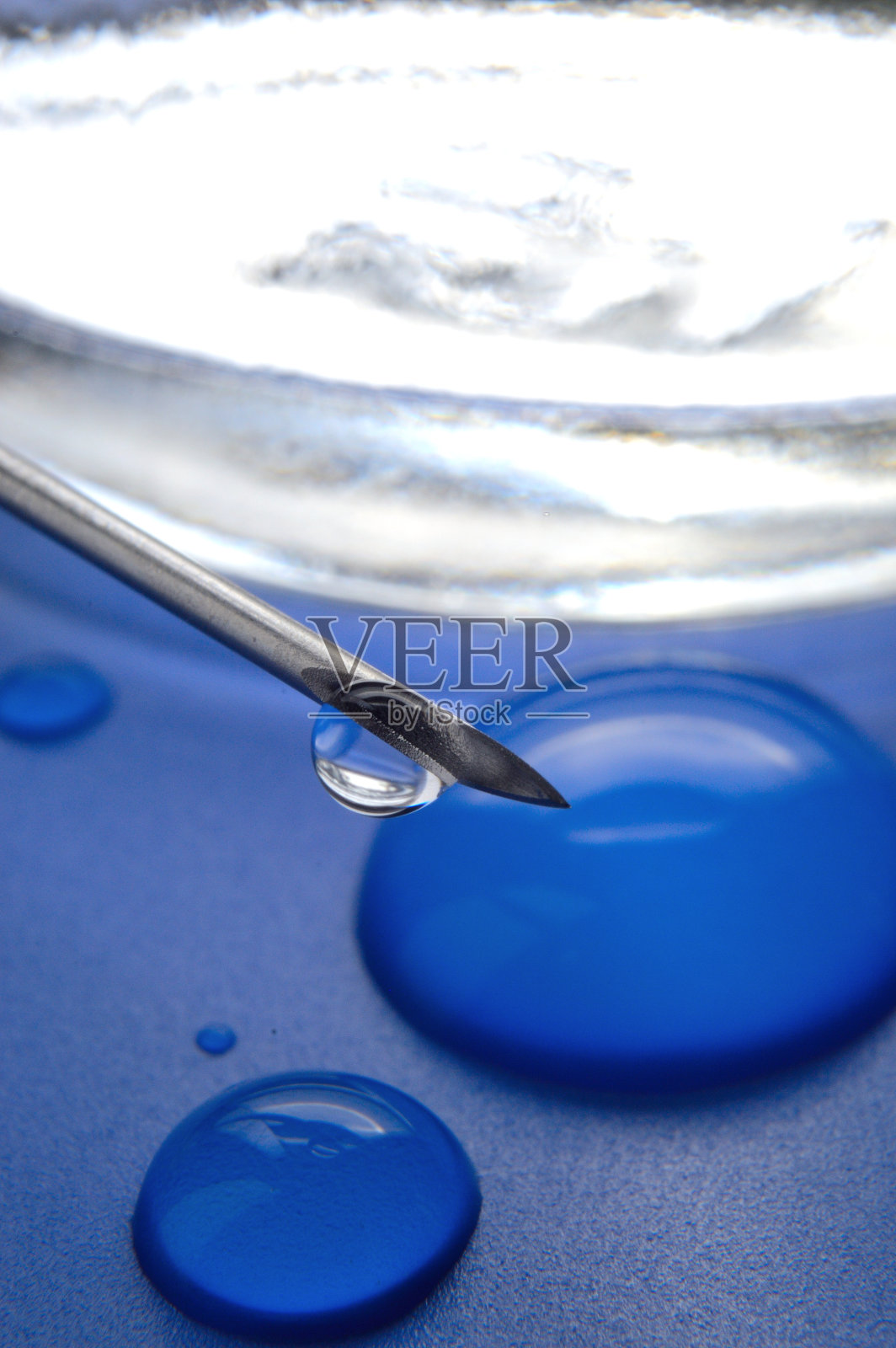 注射器针头与一滴透明物质和玻璃罐的特写。照片摄影图片