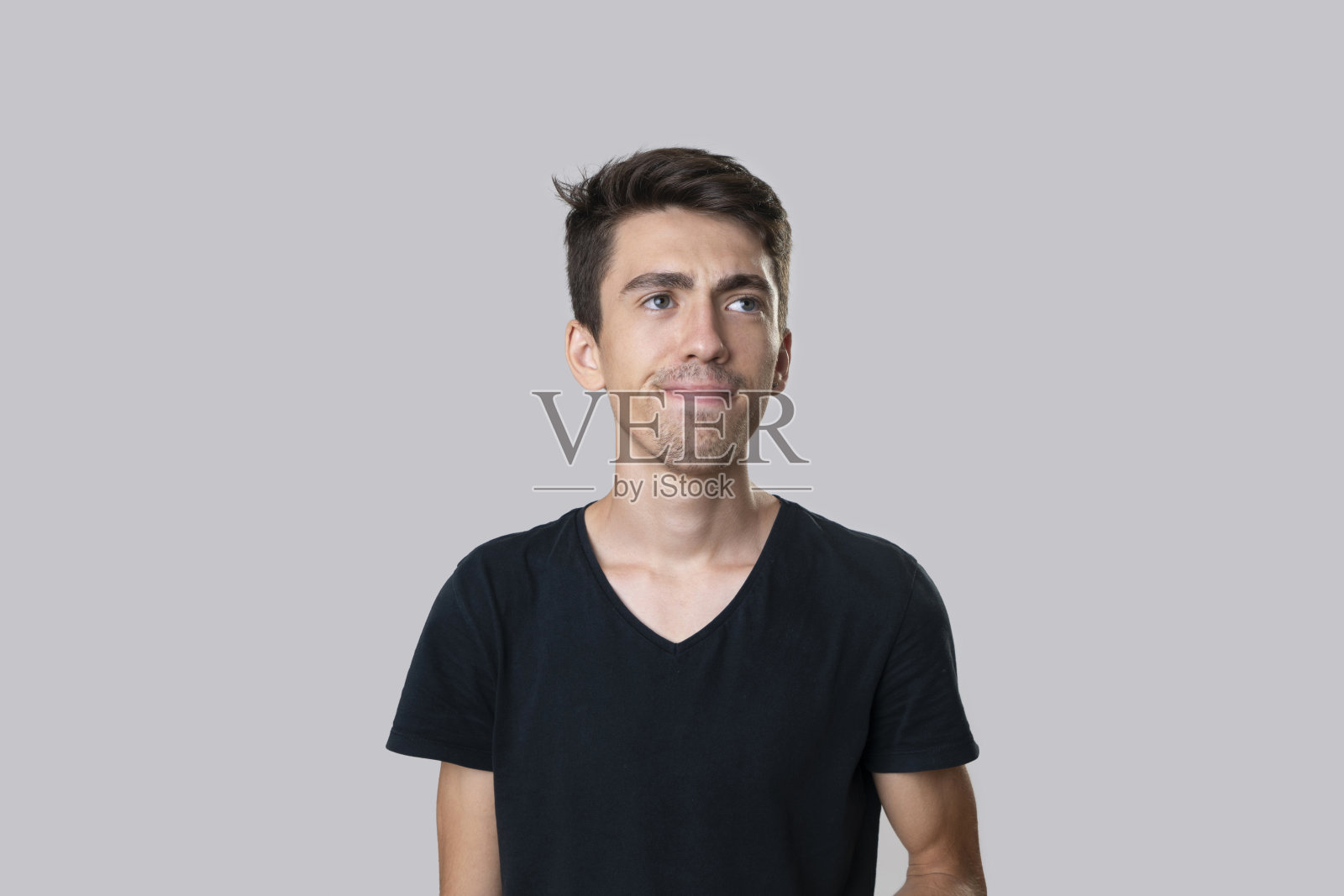 一个深思熟虑的年轻人的肖像，看起来很严肃。摄影棚拍摄，灰色背景。照片摄影图片