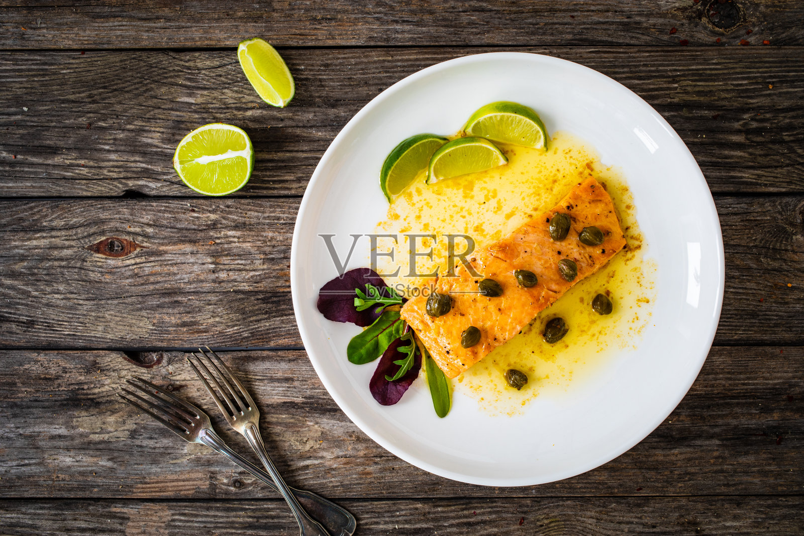 木桌上放着黄油酱炸三文鱼排配酸豆和青柠照片摄影图片