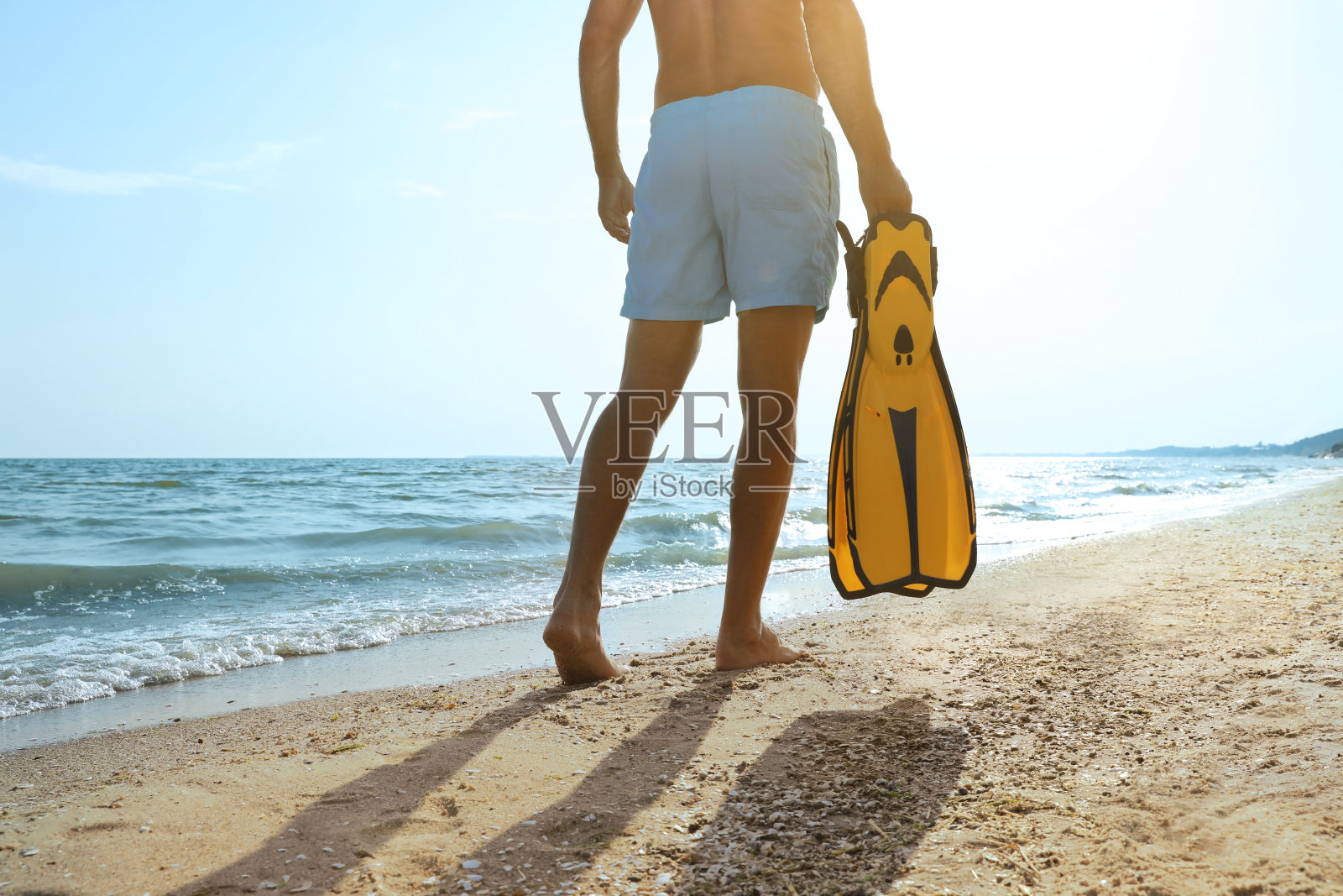 男子的后视图与鳍在海滩上行走，特写照片摄影图片