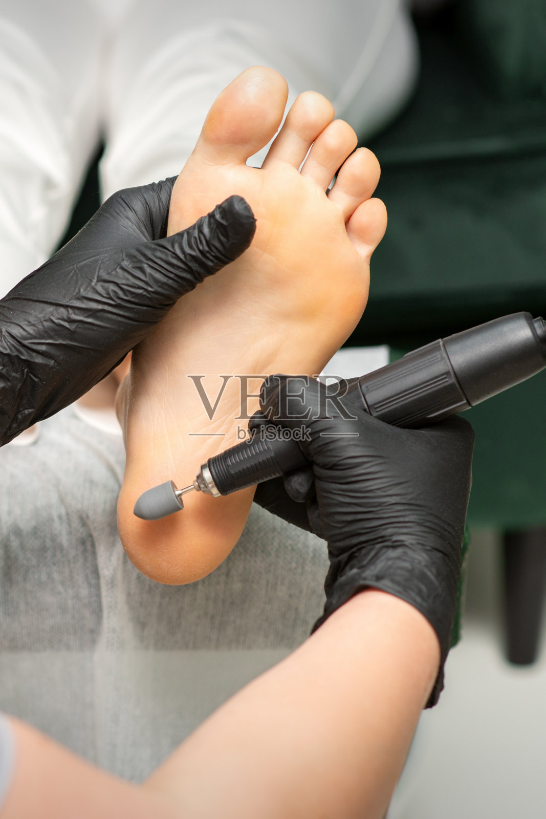 女性脚脱皮。在美容院，脚病专家戴着黑色手套，用特殊的研磨设备打磨女性脚上的老茧和玉米。照片摄影图片