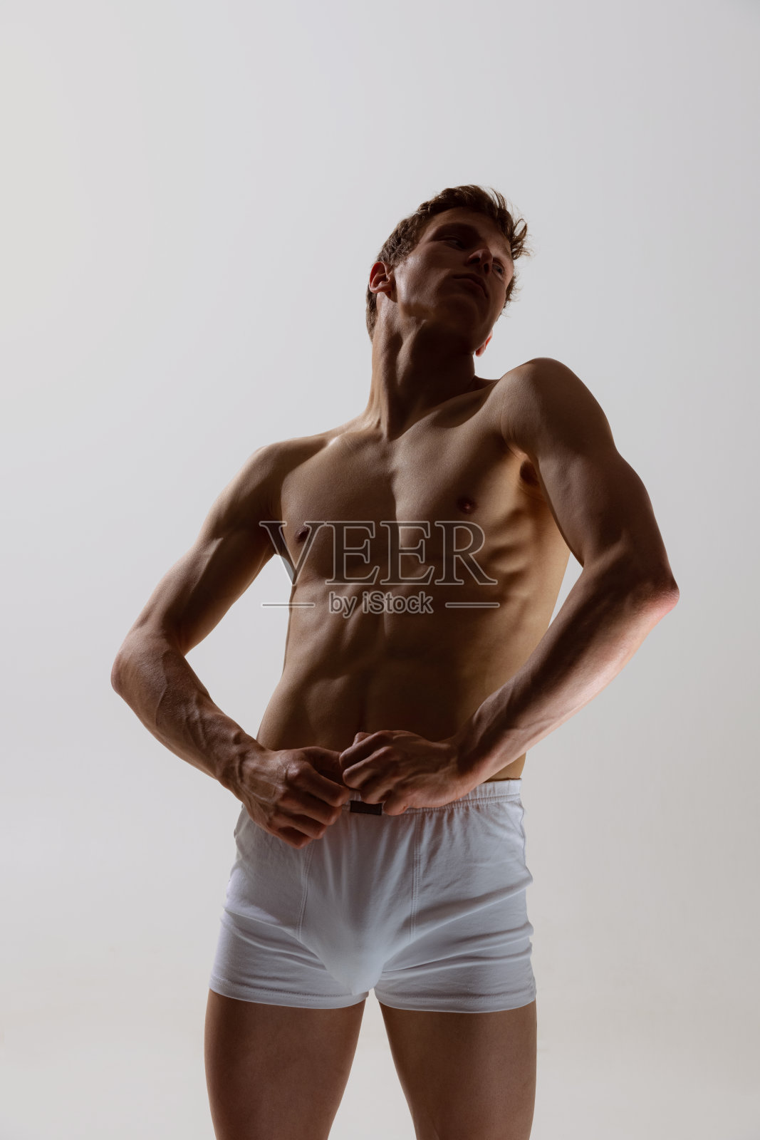 年轻英俊的肖像，赤膊运动男子穿着白色四角内裤移动顺利孤立在灰色背景。健康、健身、美容的概念。照片摄影图片