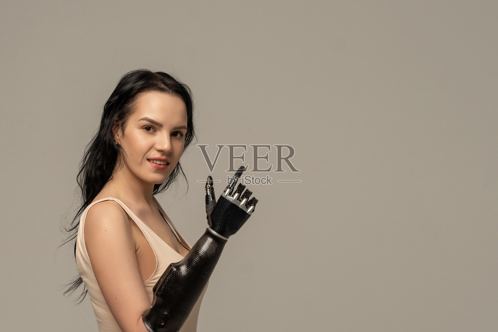 美女残疾的女人带着假肢手臂，看着右手的假手，微笑孤立在米色的背景上。美品种。积极的。本空间照片摄影图片