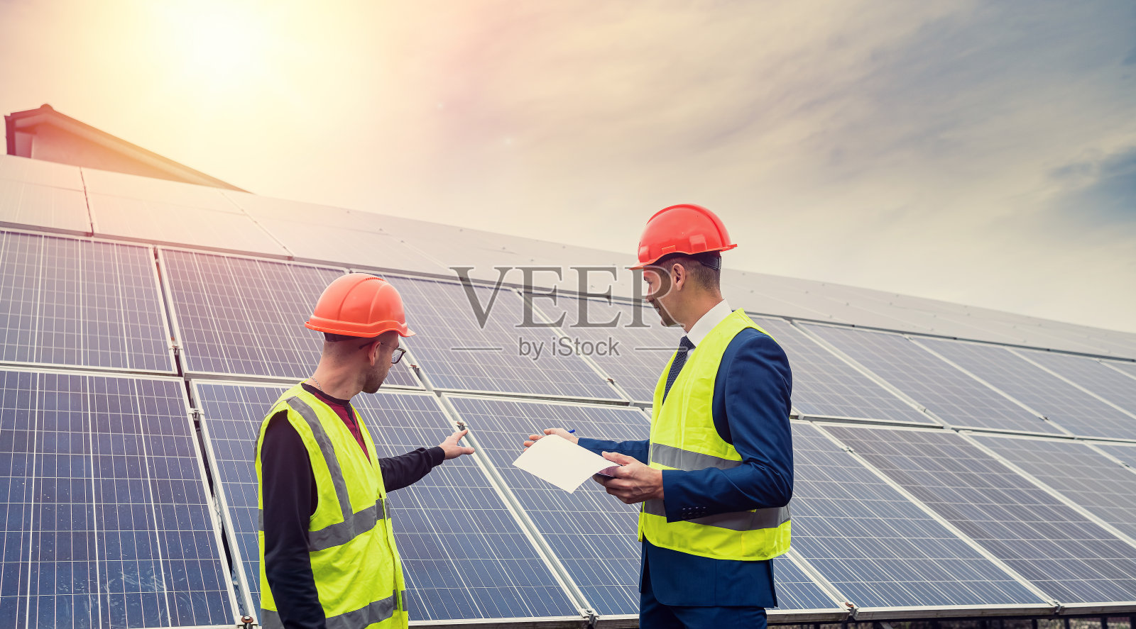 戴着安全帽、拿着文件的英俊年轻人站在新安装的面板旁边。照片摄影图片