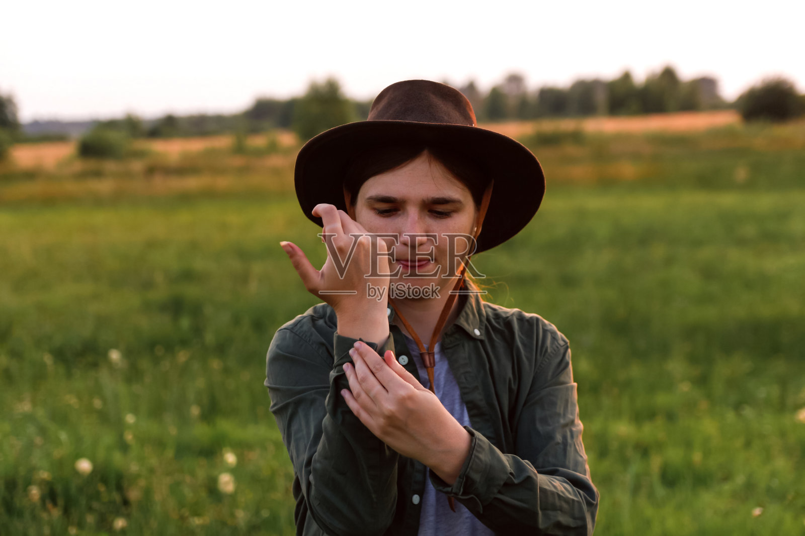 戴牛仔帽的年轻女子。田野里戴牛仔帽的女孩。日落。自然背景。特写肖像白人女孩微笑。夏季。时尚的衣服。前视图。的焦点照片摄影图片