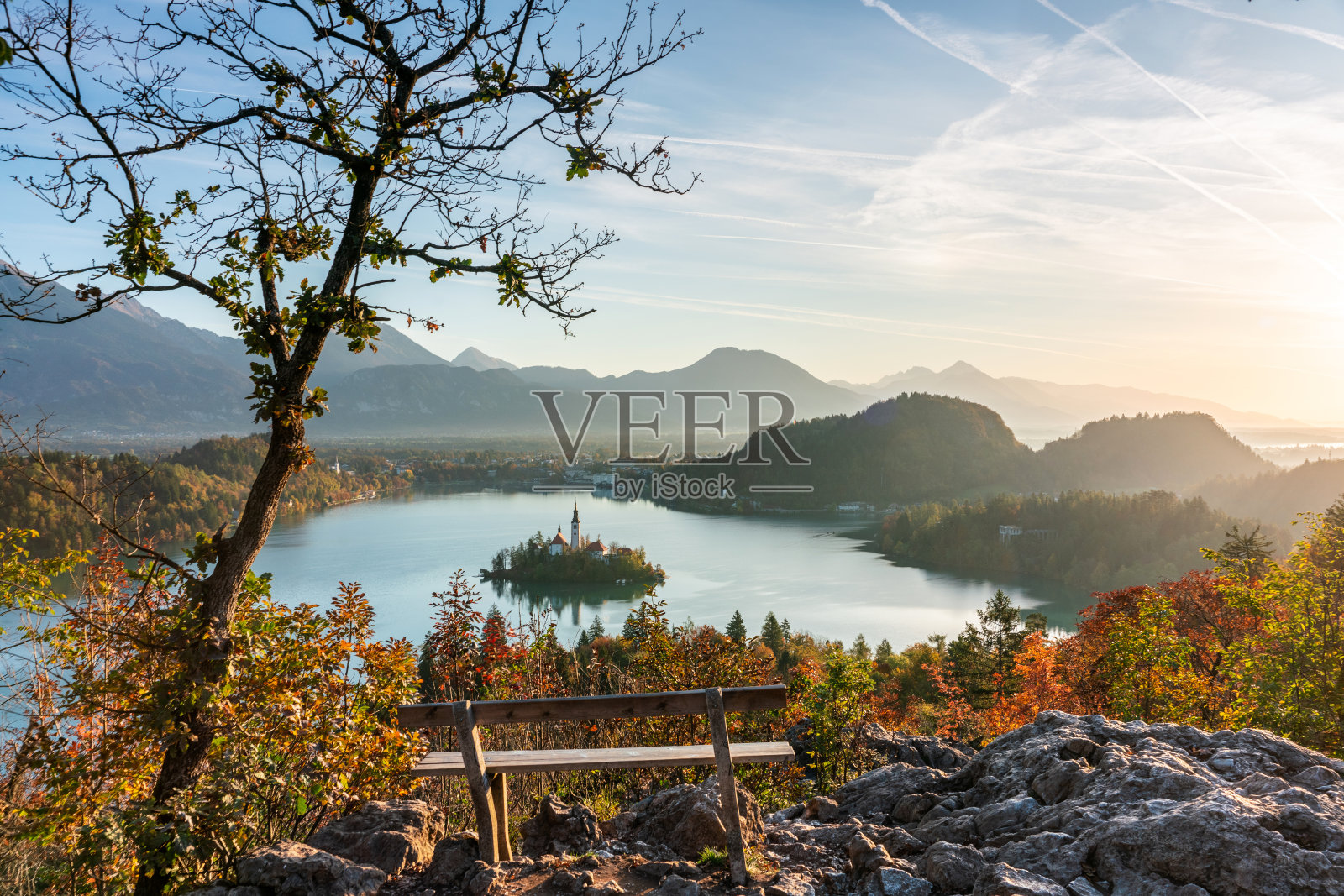 秋天的早晨，在斯洛文尼亚，一个木制的长凳在前景和山脉的背景下，令人惊叹的流血湖的景色。旅行和放松的概念照片摄影图片