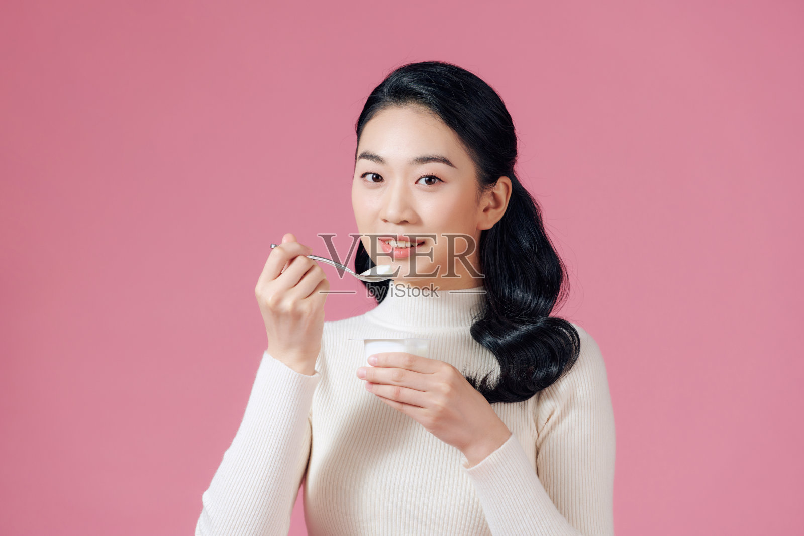 年轻美丽微笑的女人吃新鲜的酸奶上粉红色照片摄影图片