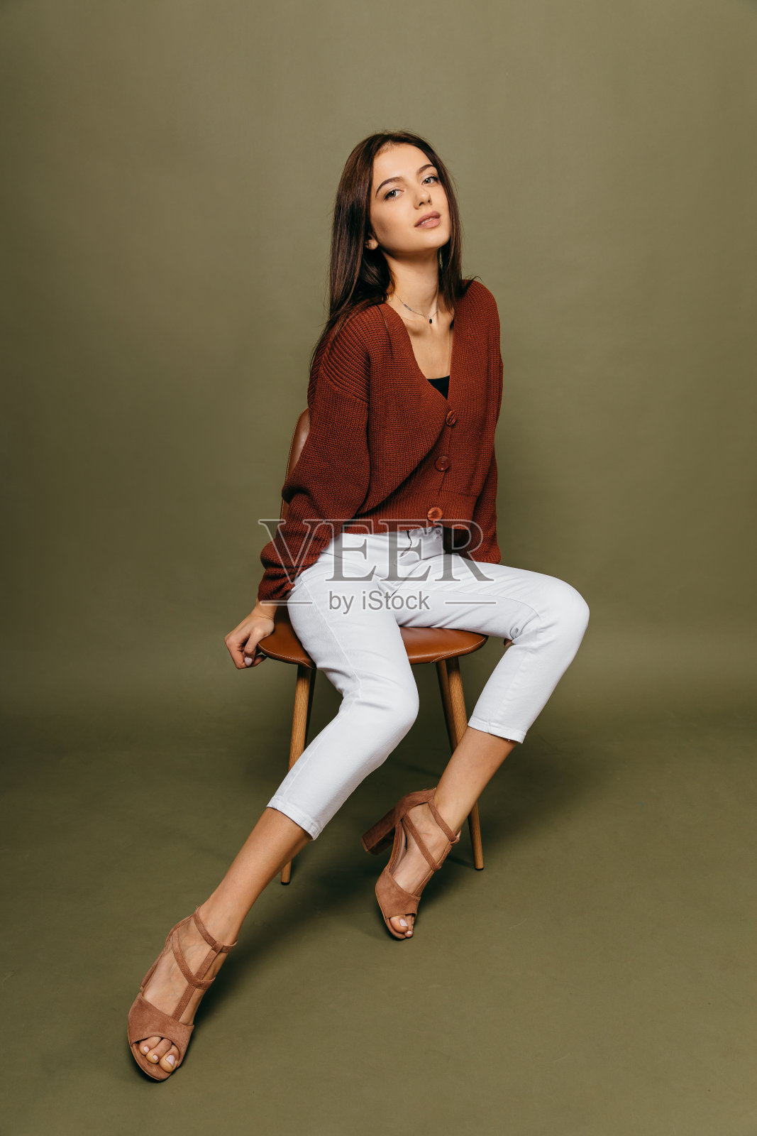 惊人的年轻女孩的肖像与一个美丽的人物坐在椅子上对橄榄色的背景在工作室。照片摄影图片