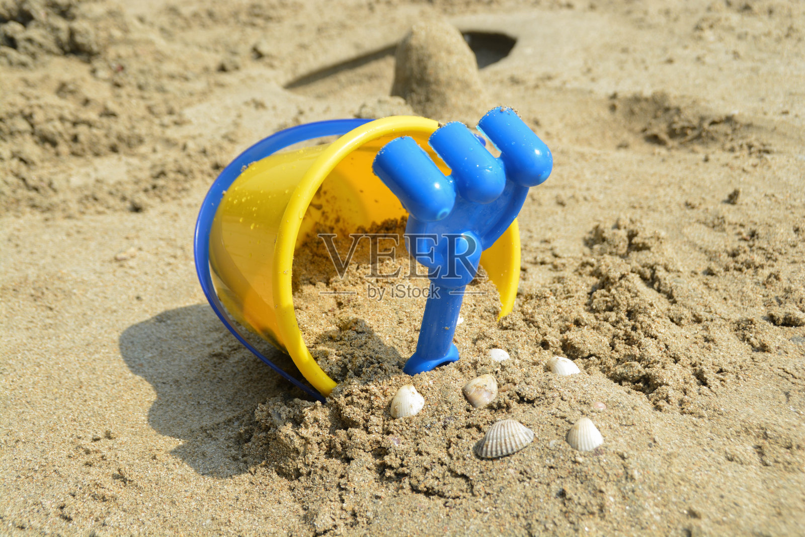 黄色的水桶孩子玩具和蓝色的耙子。还有装着贝壳的桶里的沙子。照片摄影图片