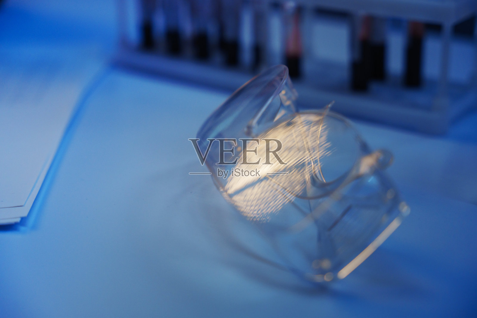 一副防护眼镜放在实验室的桌子上，背景中有一个试管，试管中有血液照片摄影图片