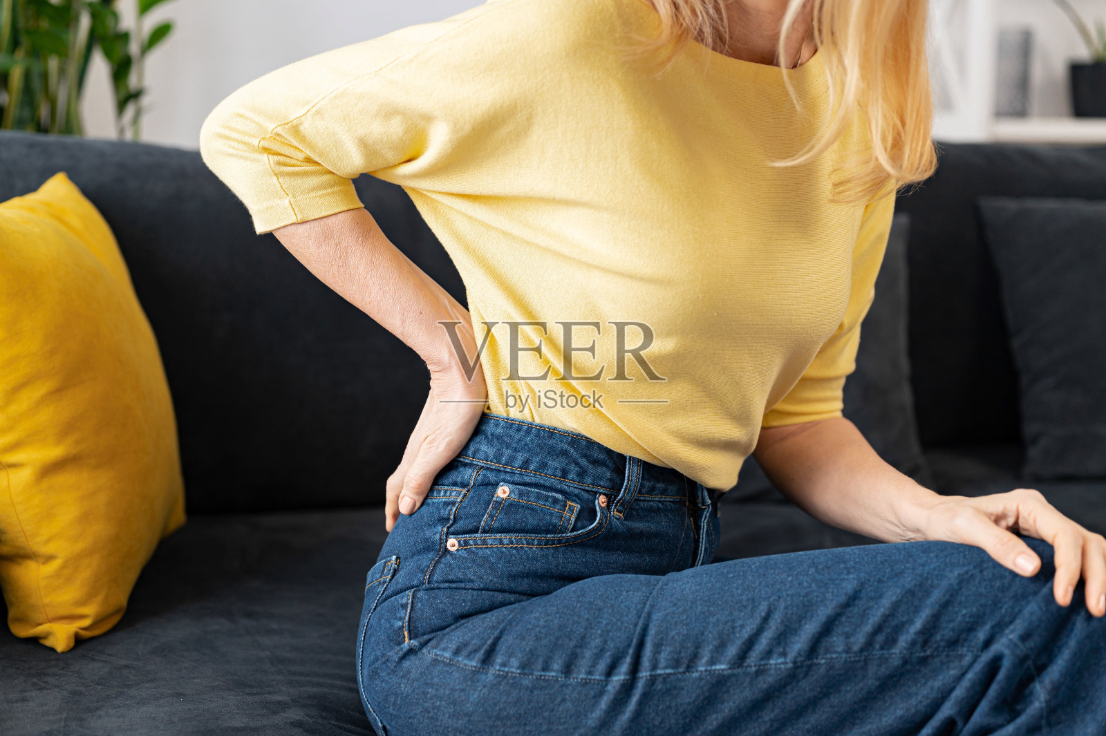 裁剪的观点的资深妇女感到腰部刺痛坐在家里的沙发上照片摄影图片