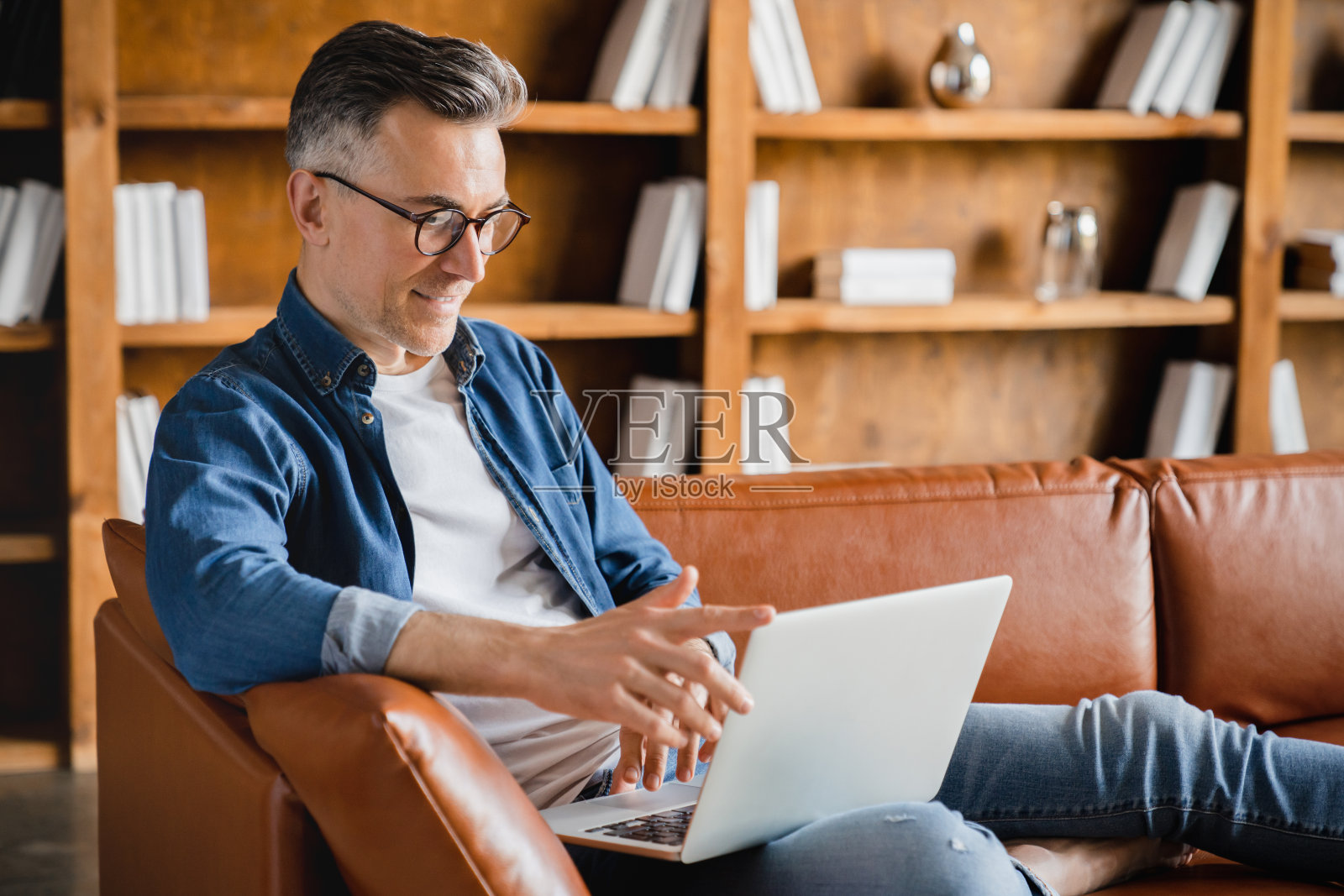 远程远程工作。高加索成熟中年男性，商人，自由职业者，用笔记本电脑工作，观看网络研讨会，在线学习，在家办公的沙发上多任务处理照片摄影图片