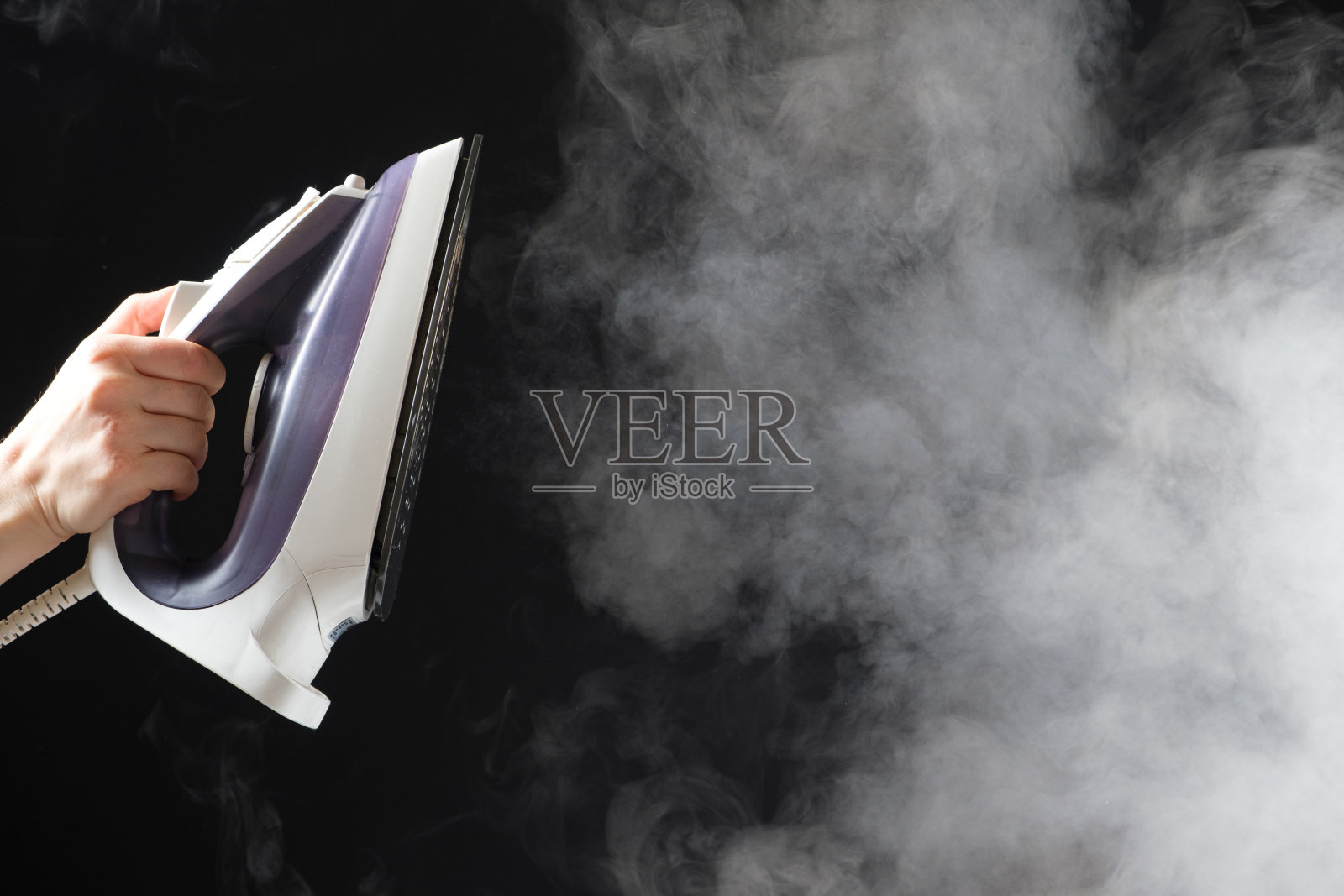 带有蒸汽发生器的熨斗在黑色背景上喷射出白色的蒸汽。照片摄影图片