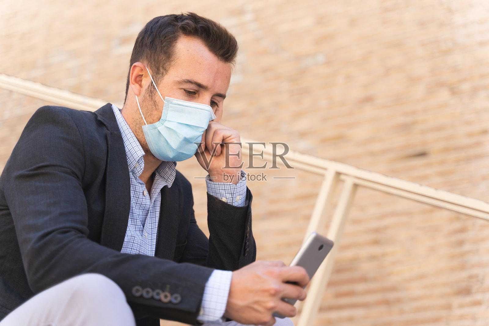 戴着口罩的商人坐在街上，一边用手机，一边若有所思照片摄影图片