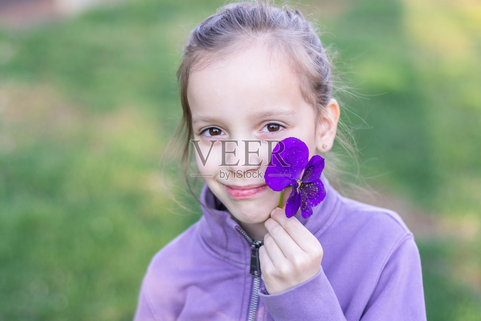 孩子拿着紫色的花，看着镜头照片摄影图片