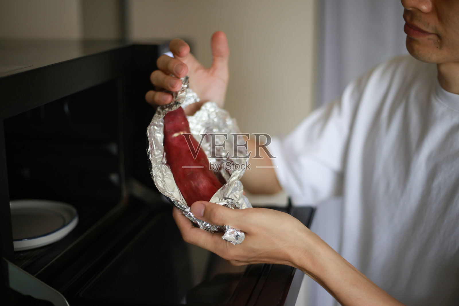 一个用铝箔包红薯并试图用微波炉加热的男人照片摄影图片