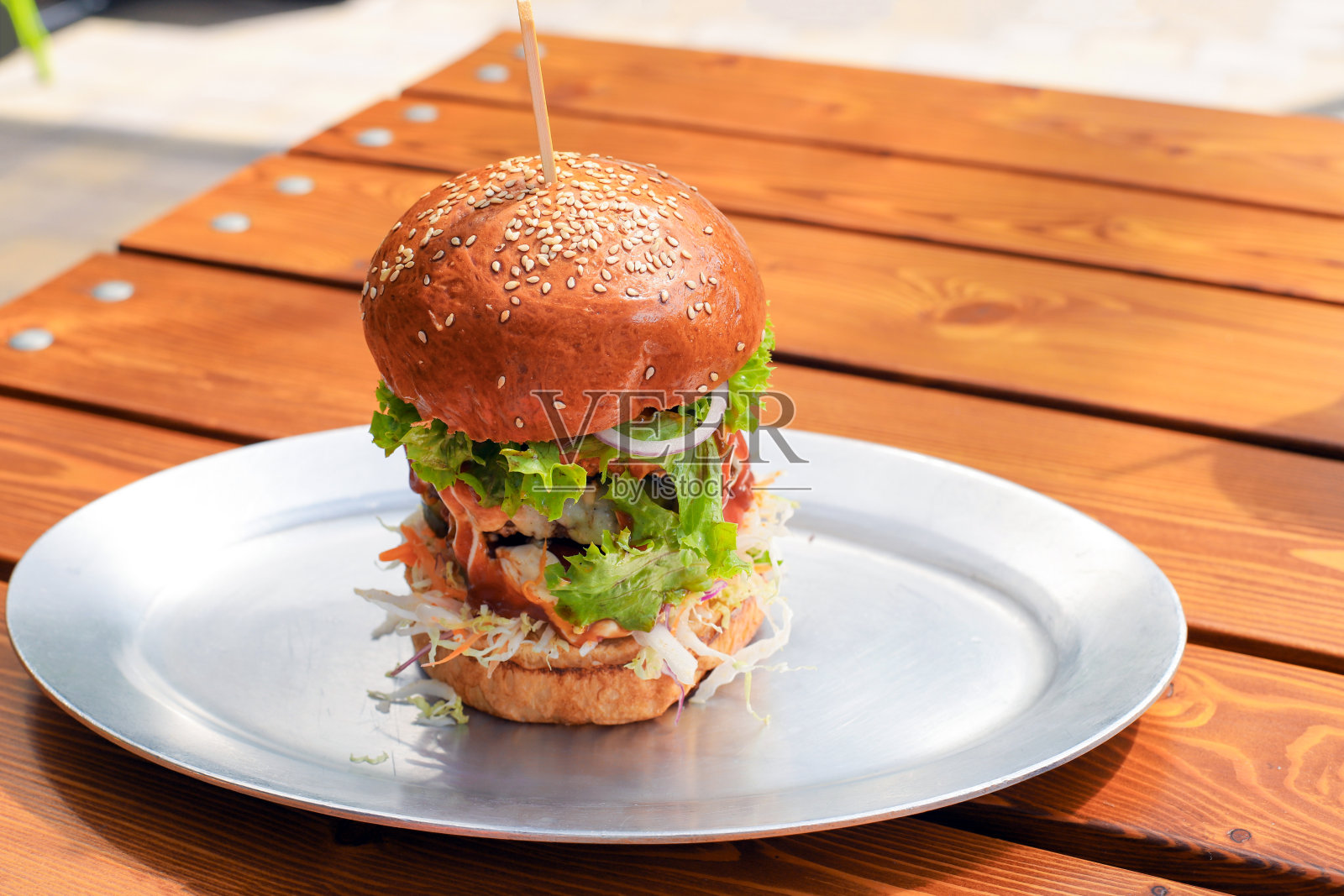 高高的大的美味汉堡或牛肉汉堡与蔬菜和酱在金属盘子上的木制桌子。在晴天吃早午餐。特写，复印空间，正面，快餐。照片摄影图片