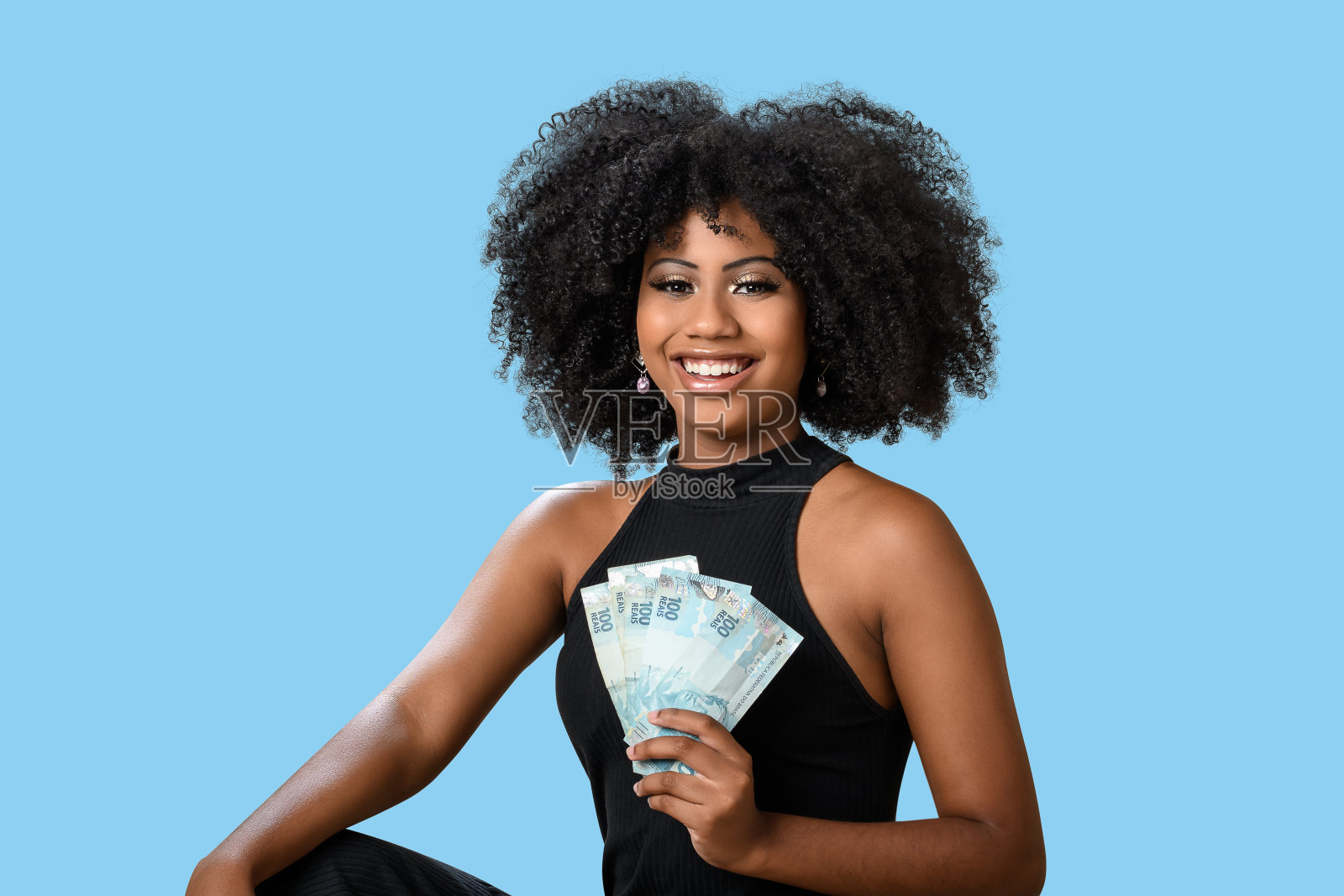 年轻的黑人妇女微笑着拿着巴西钞票，非常惊讶，文字、人物、广告概念的空间，孤立在蓝色背景上。照片摄影图片