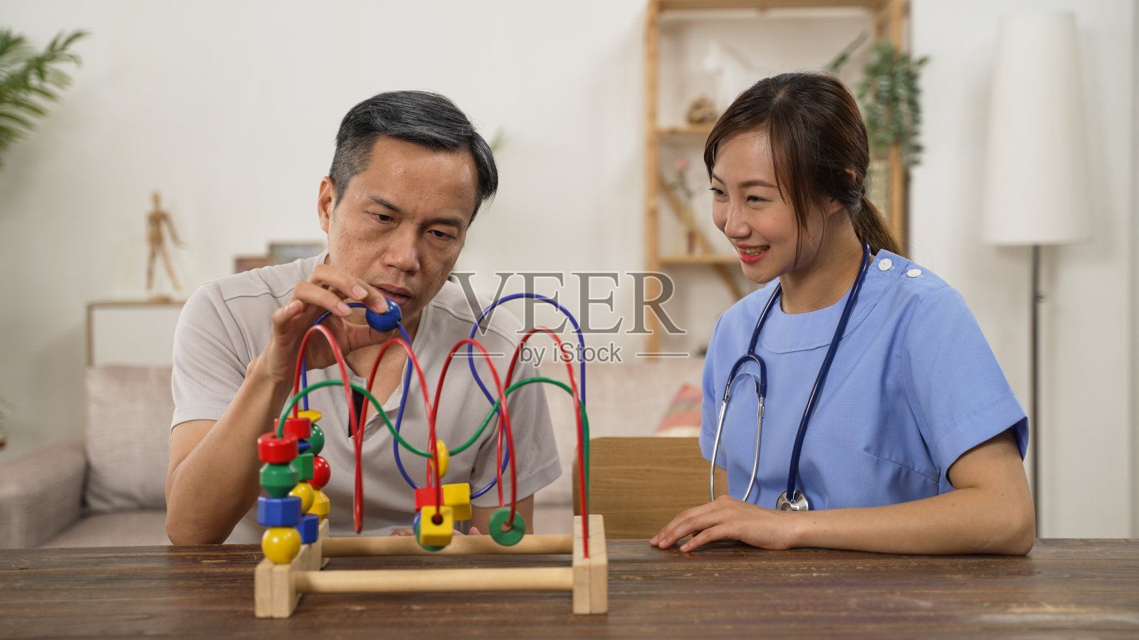 有爱心的日本女性护理员在家里做理疗的时候，看着老年帕金森患者用珠子迷宫练习他的手部肌肉。照片摄影图片