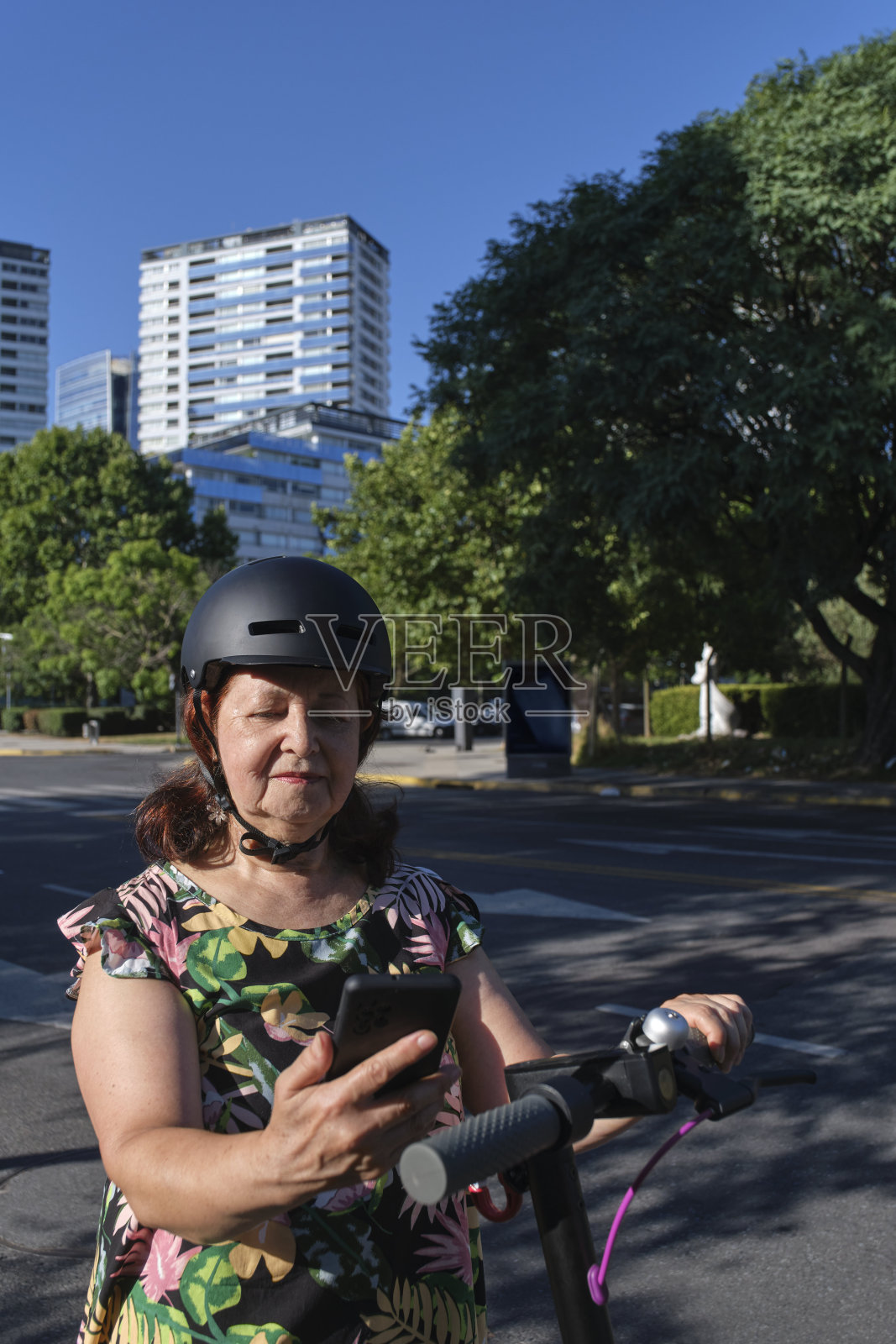 一个戴着头盔的成熟女人在骑电动摩托车前看她的手机照片摄影图片