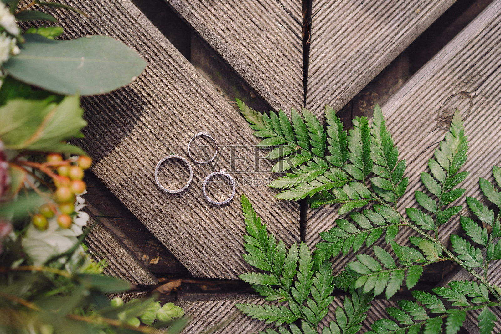 花束，结婚戒指和订婚戒指的木制背景，绿色植物和蕨类植物的叶子。照片摄影图片