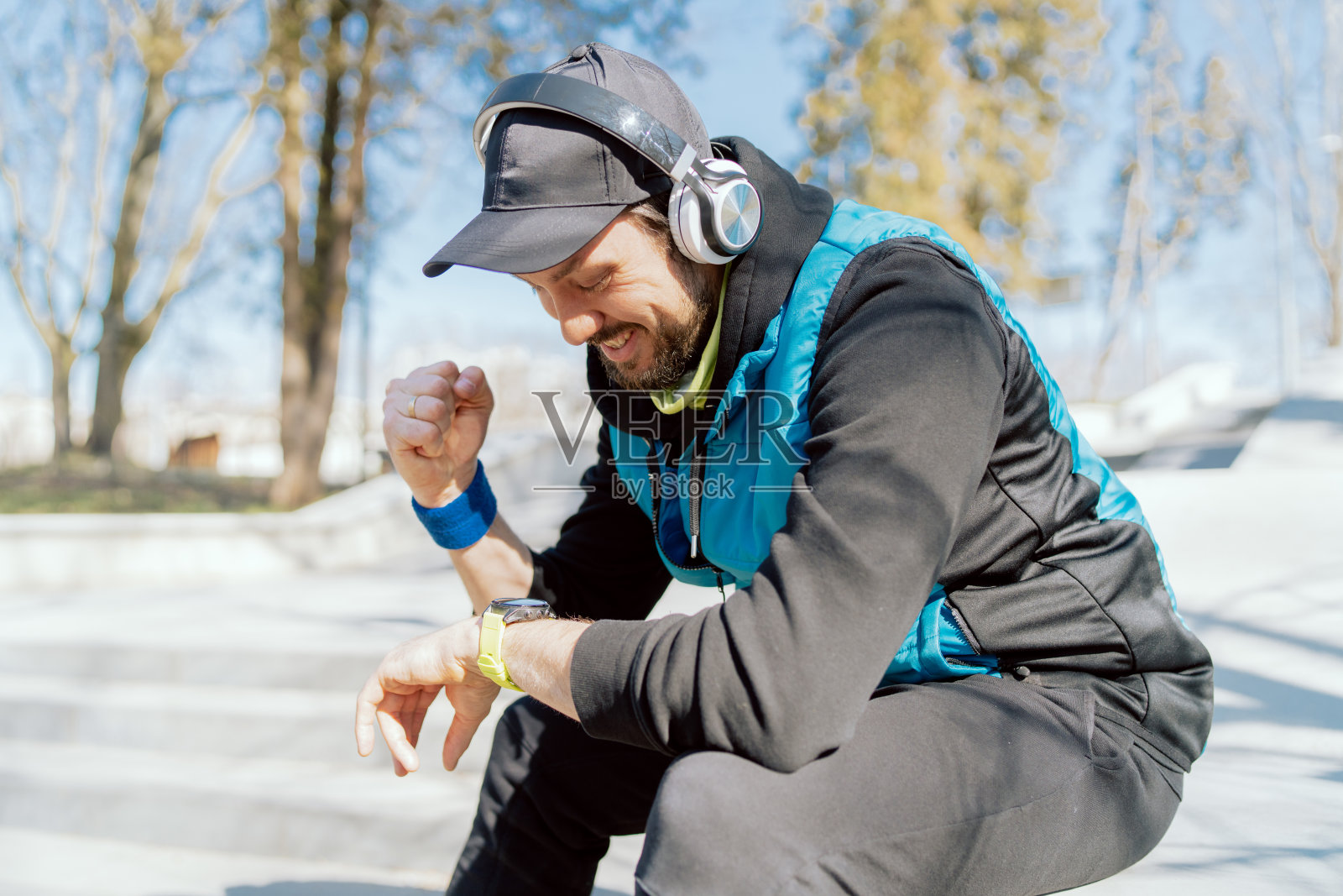 一名男运动员在晨跑时对自己的成绩很满意，微笑着，在智能手表上检查参数，高兴地握紧拳头，耳机里放着激励人心的音乐照片摄影图片