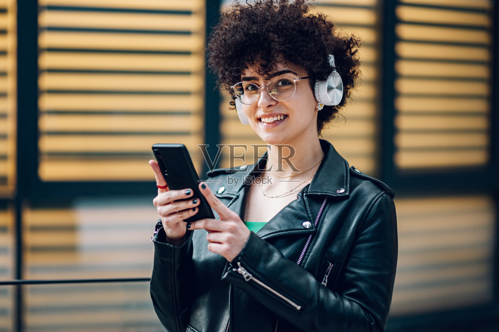 女人走在城市的街道上，戴着手机和耳机照片摄影图片