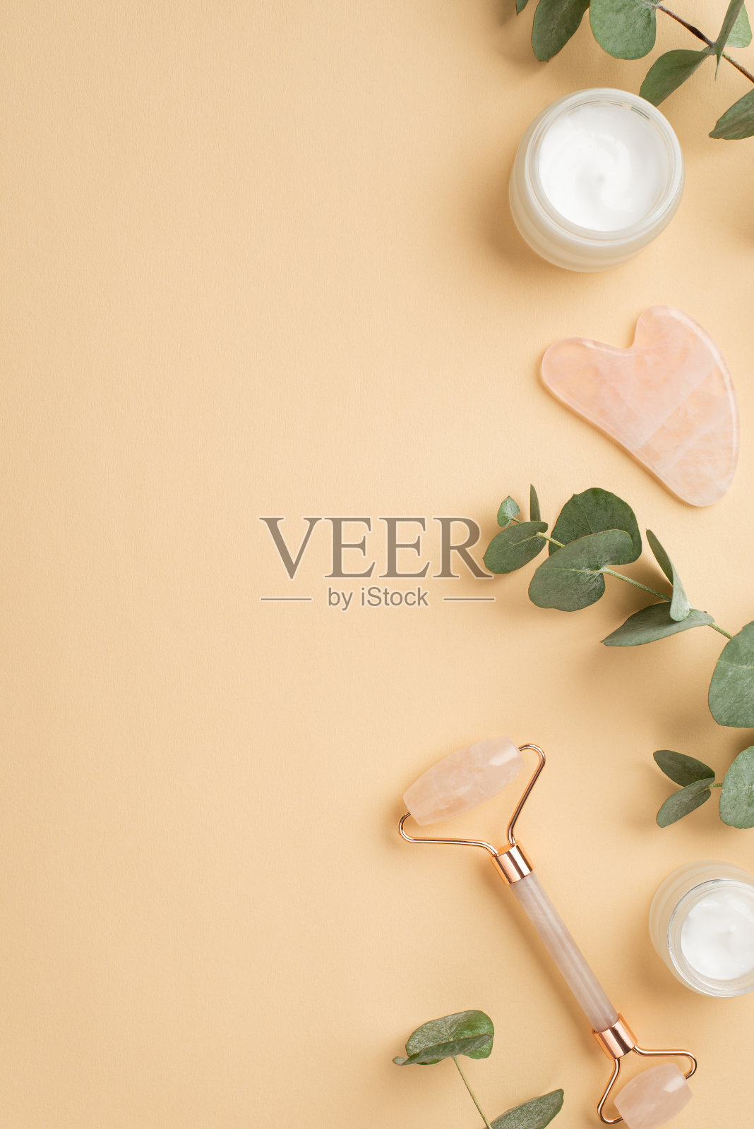 护肤概念。俯视图垂直照片的玫瑰石英辊挂沙霜瓶和桉树叶孤立粉彩米色背景与空的空间照片摄影图片