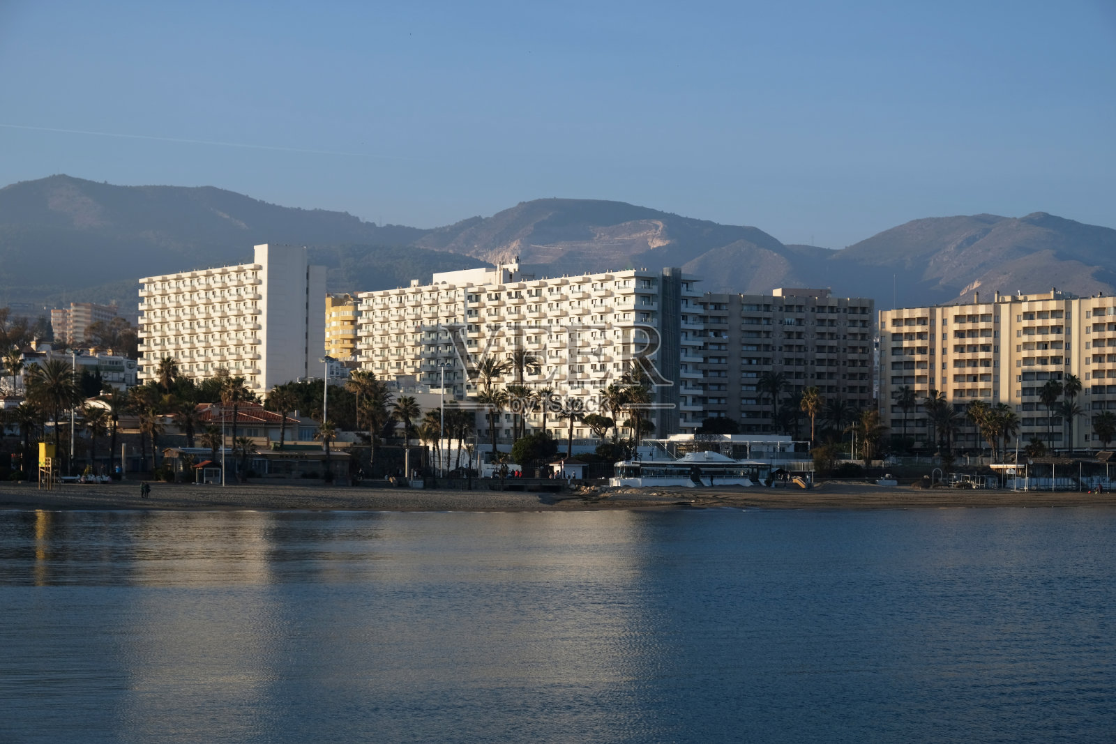 在马拉加，安达卢西亚，西班牙地中海海岸的高层度假酒店或住宅建筑的观点。沙滩，棕榈树，蓝色的大海，蓝天和山脉的景色。房地产的概念。照片摄影图片