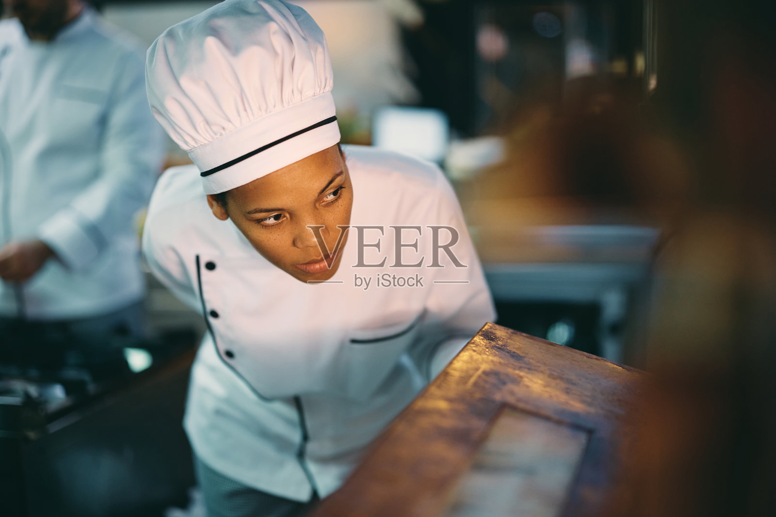 非裔美国专业厨师在餐馆工作时检查烤箱里的食物。照片摄影图片