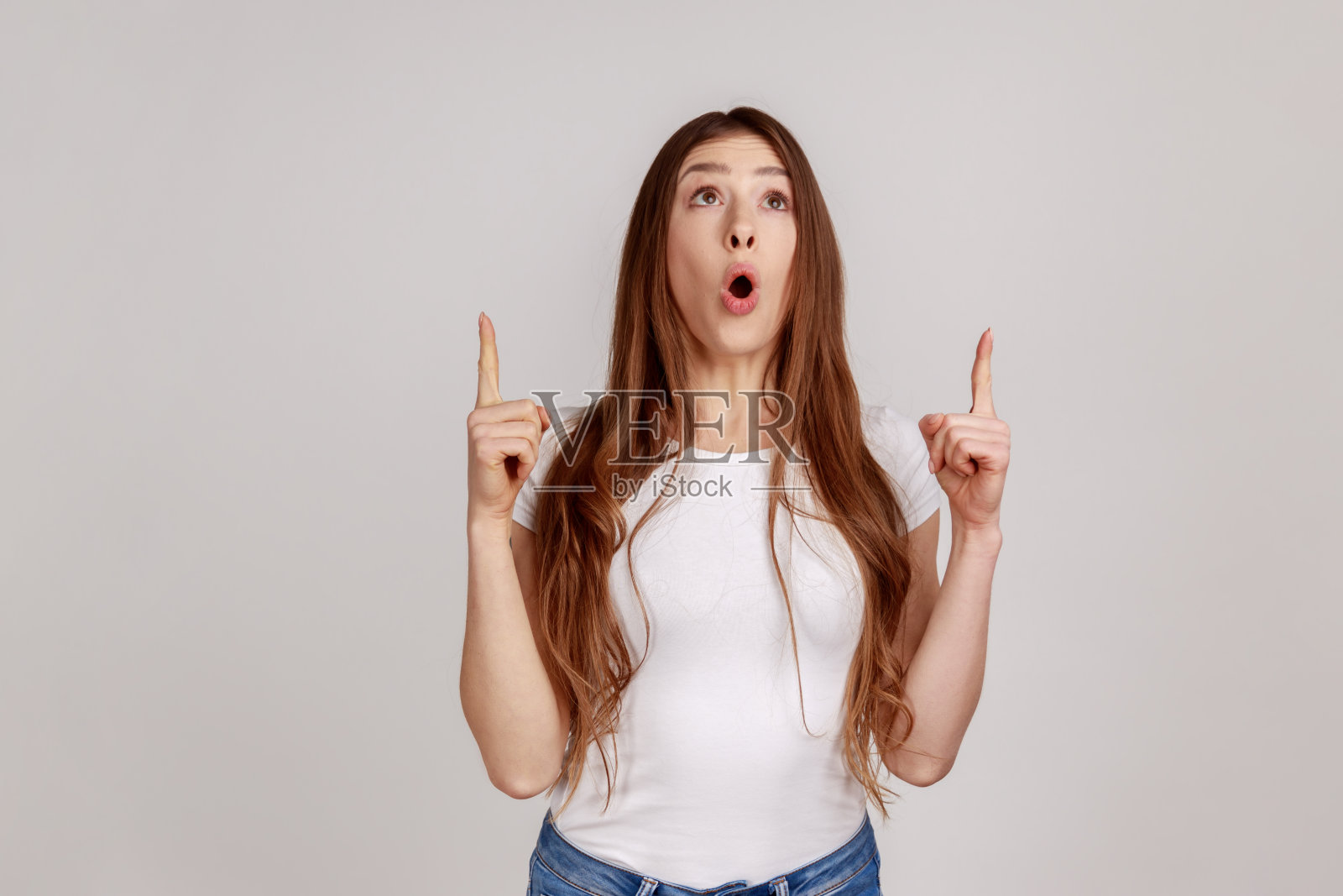 女人指着头顶上空白的复印空间，惊讶地向上看，看到了空墙，照片摄影图片