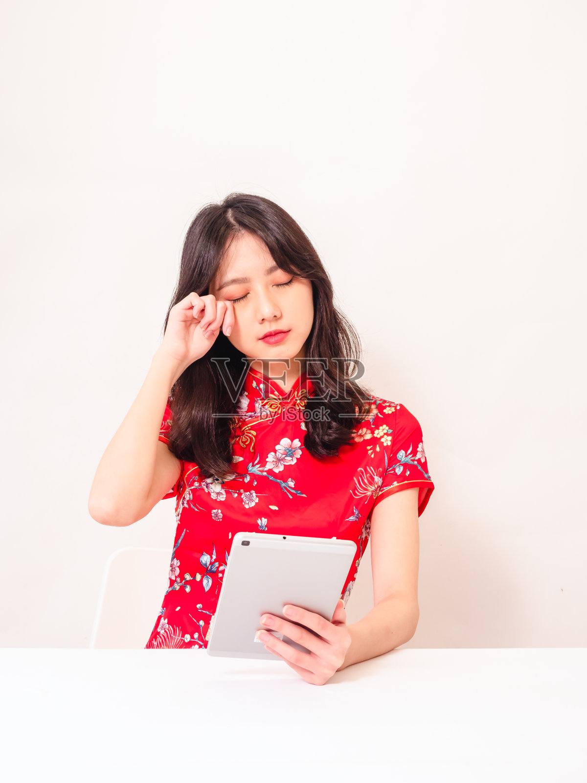 年轻的亚洲女性穿着传统旗袍，感觉疲惫和不安后，使用平板和揉眼睛不适孤立在白色背景。照片摄影图片