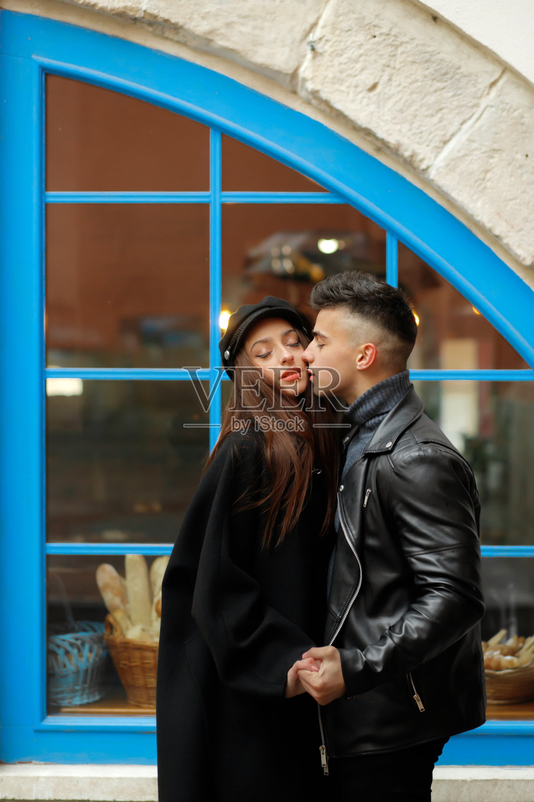雨中相爱的可爱情侣。美丽的女孩拥抱着她的男朋友，背景是蓝色的窗户照片摄影图片