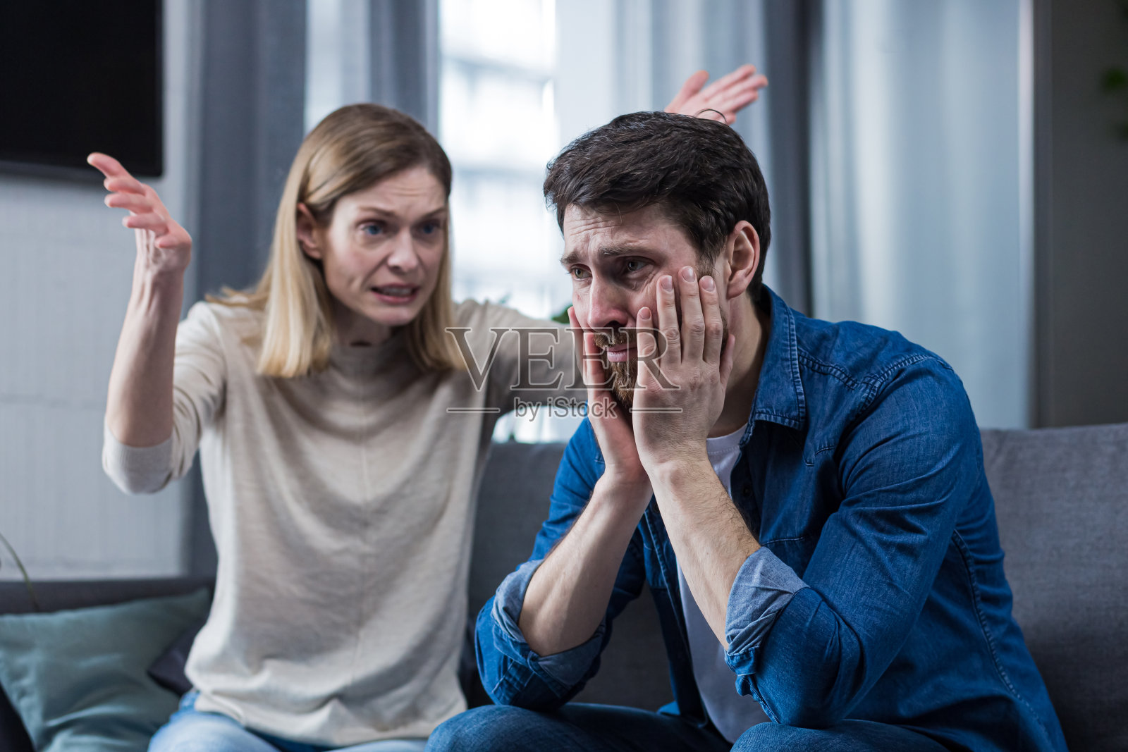 家庭吵架，女人对着输的丈夫大吼大叫，夫妻俩坐在家里客厅的沙发上照片摄影图片