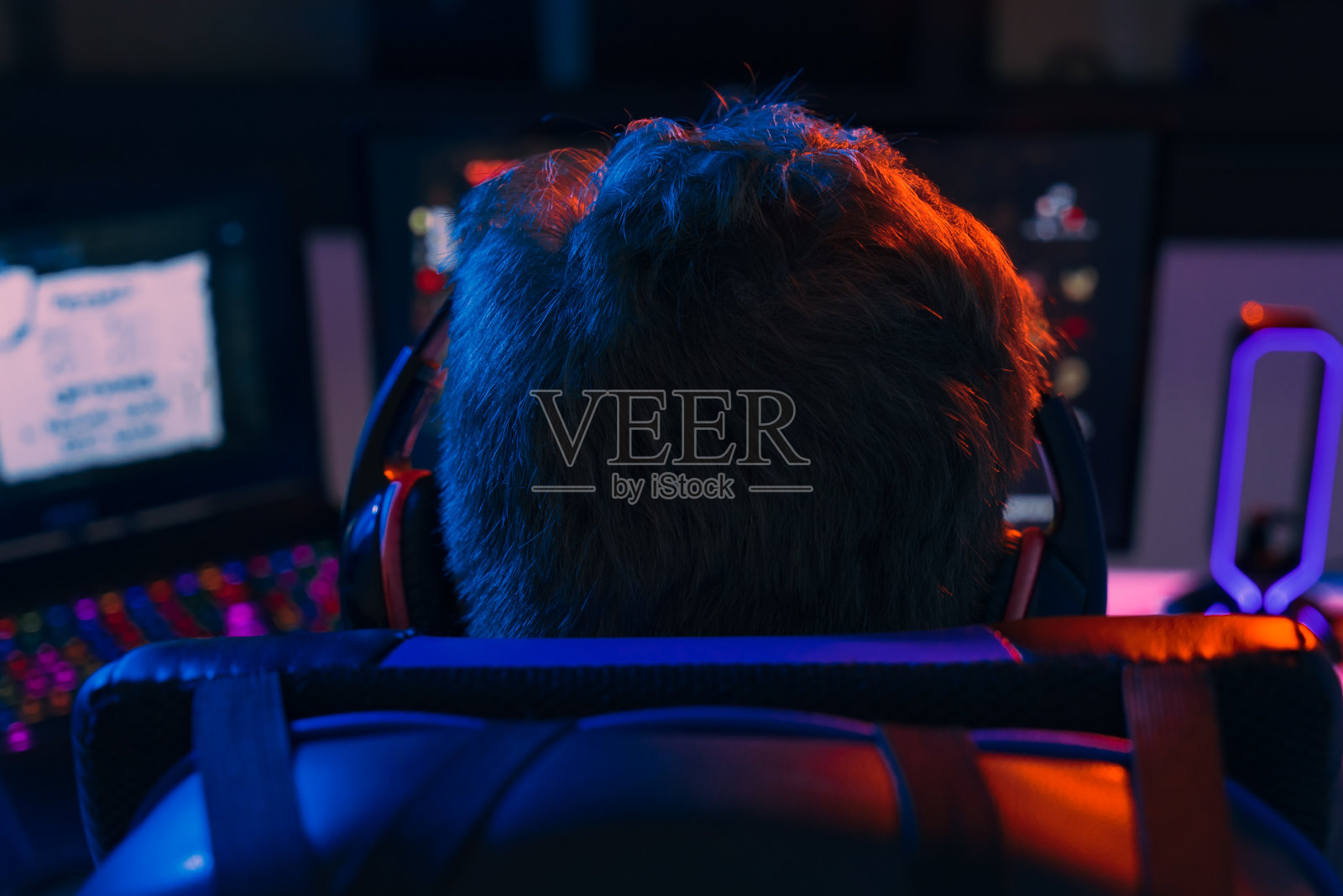 一个戴着耳机沉迷于电脑游戏的年轻人的背影。照片摄影图片