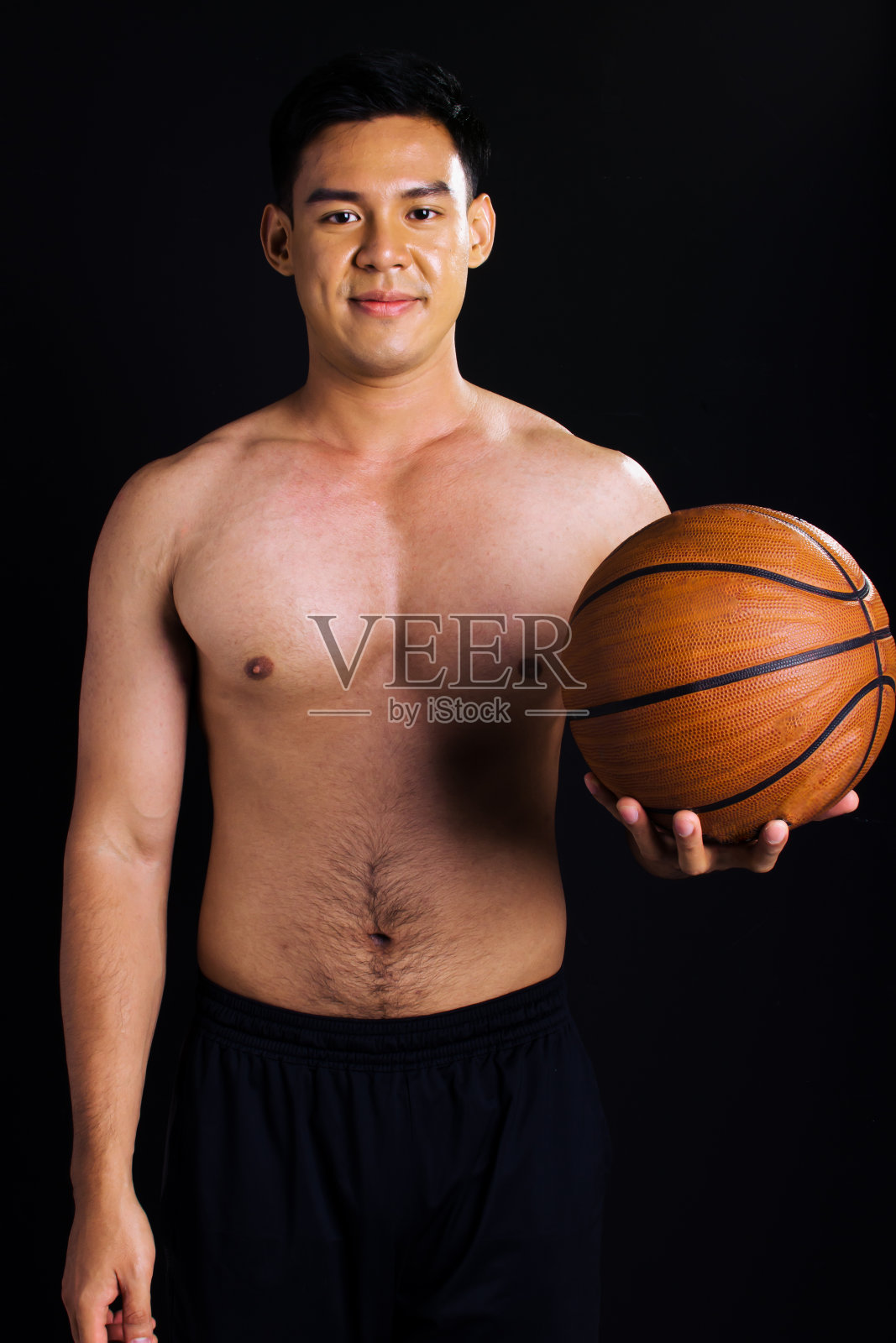 英俊的亚洲年轻肌肉男子的肖像微笑与信心，站和持有篮球上孤立的黑色背景剪纸。体育与健康理念。照片摄影图片